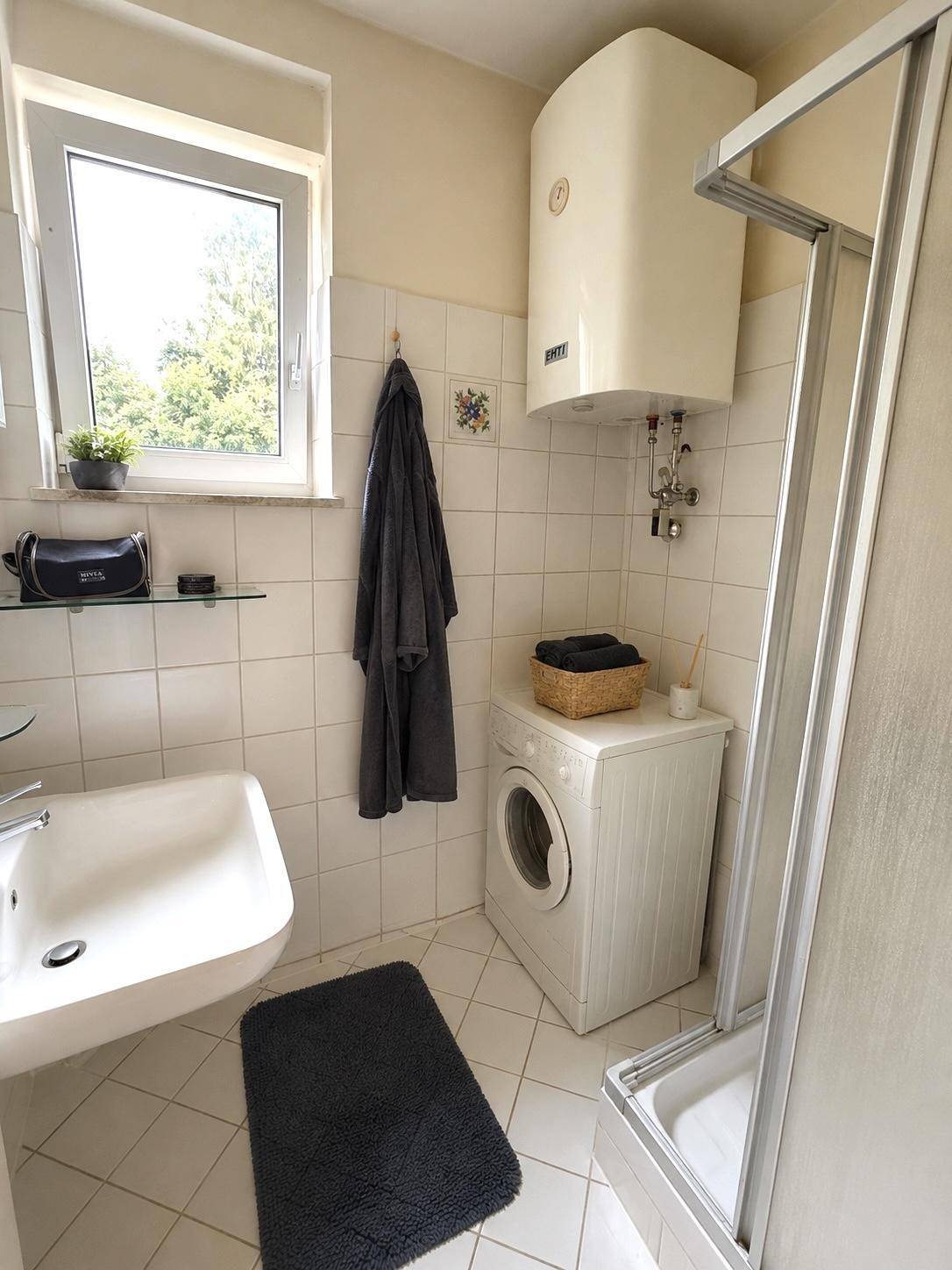 Funktionales Badezimmer mit Dusche, Waschbecken, Fenster und Waschmaschine.