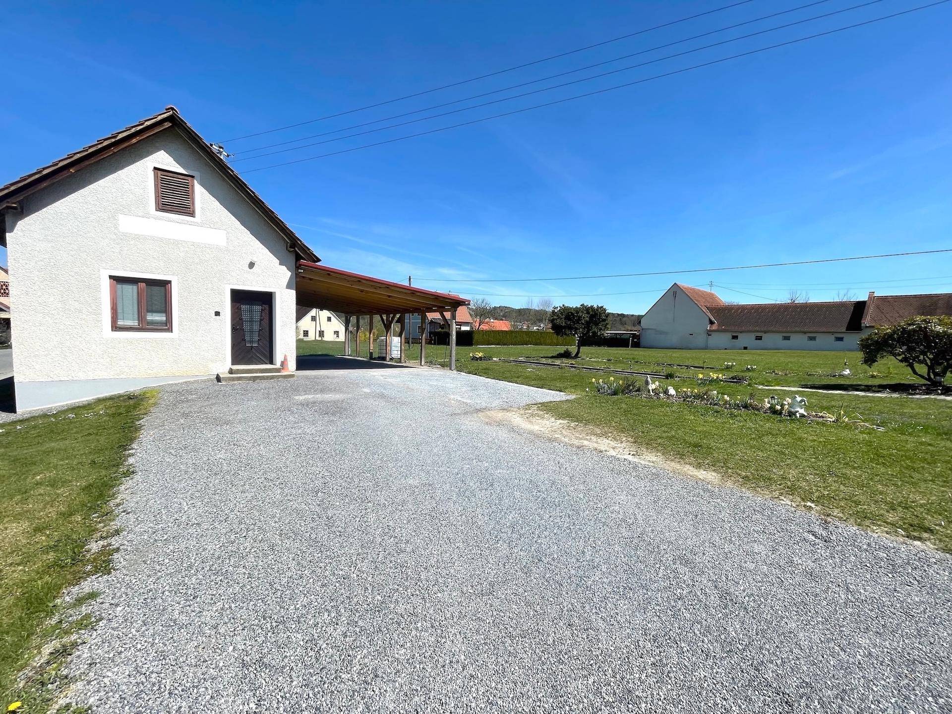 Einfahrt zum Haus mit Kiesfläche und angrenzendem Garten.