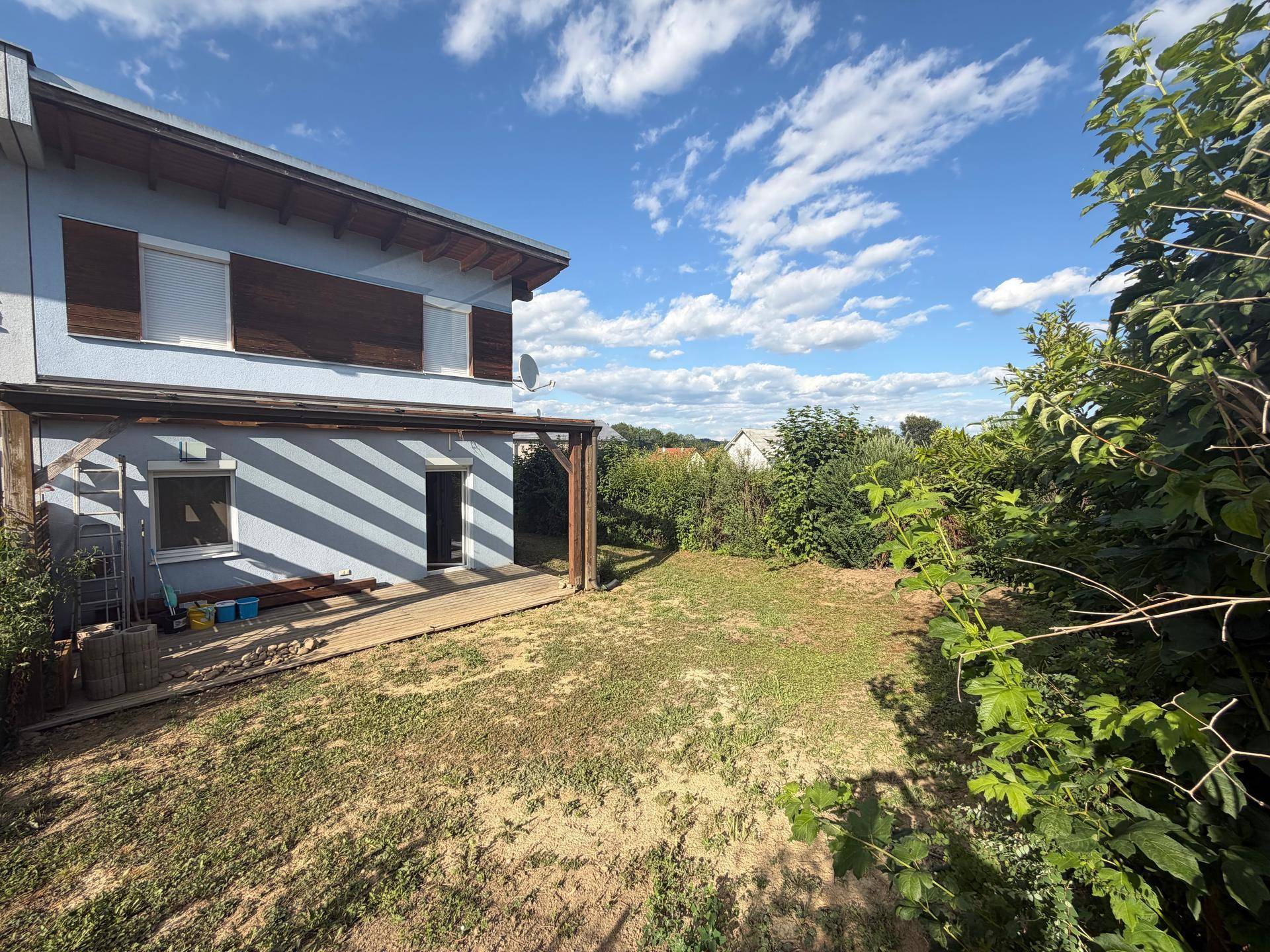 Rückseite des Hauses mit Holzterrasse und großem Gartenbereich unter blauem Himmel.