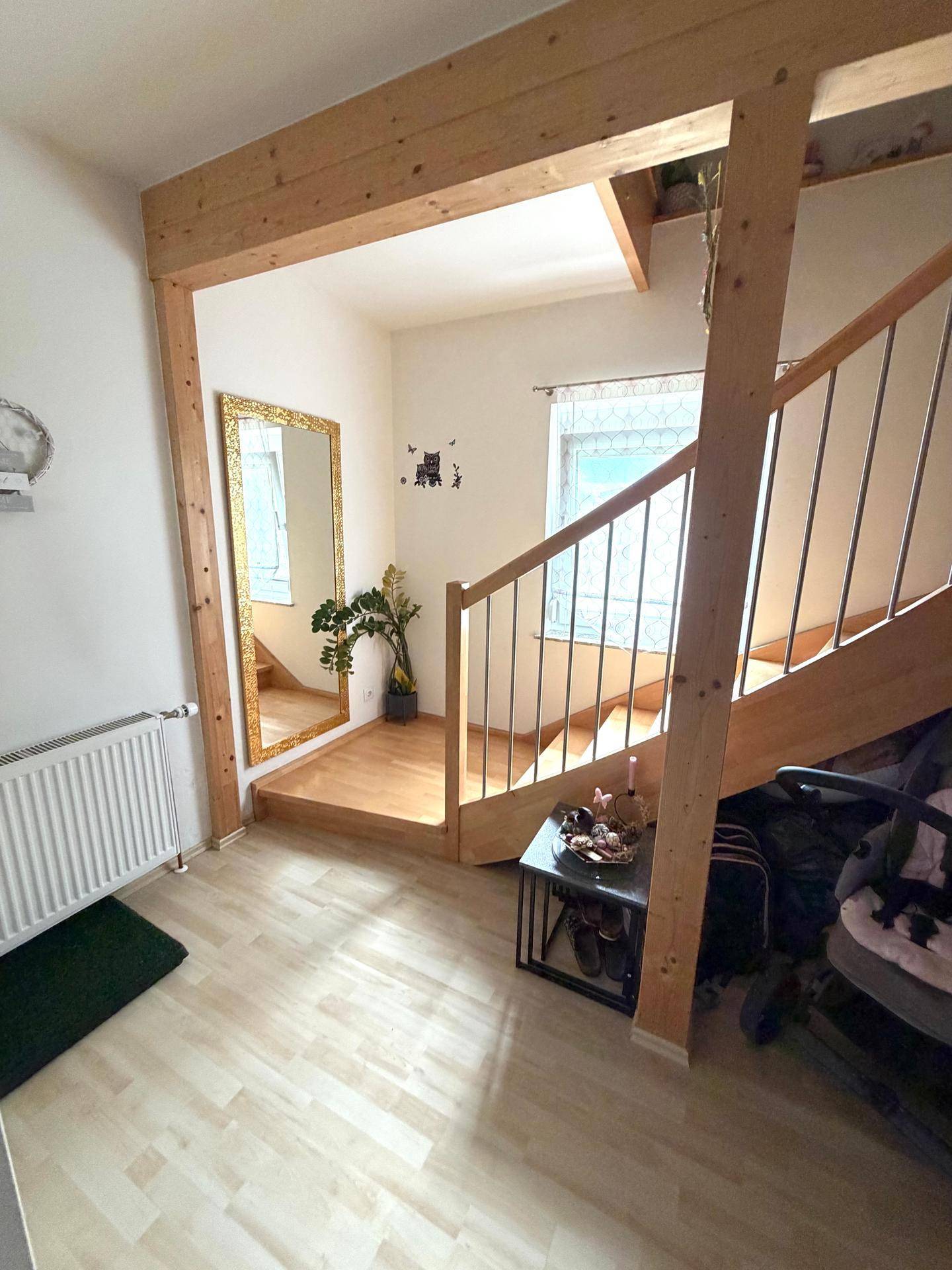 Heller Eingangsbereich mit Holztreppe, Laminatboden und einem großen Spiegel, der den Raum erweitert.