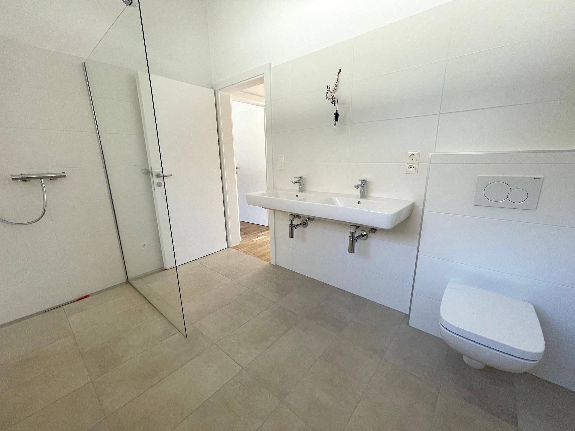 Modernes Badezimmer mit Doppelwaschbecken, wandhängendem WC und begehbarer Dusche.