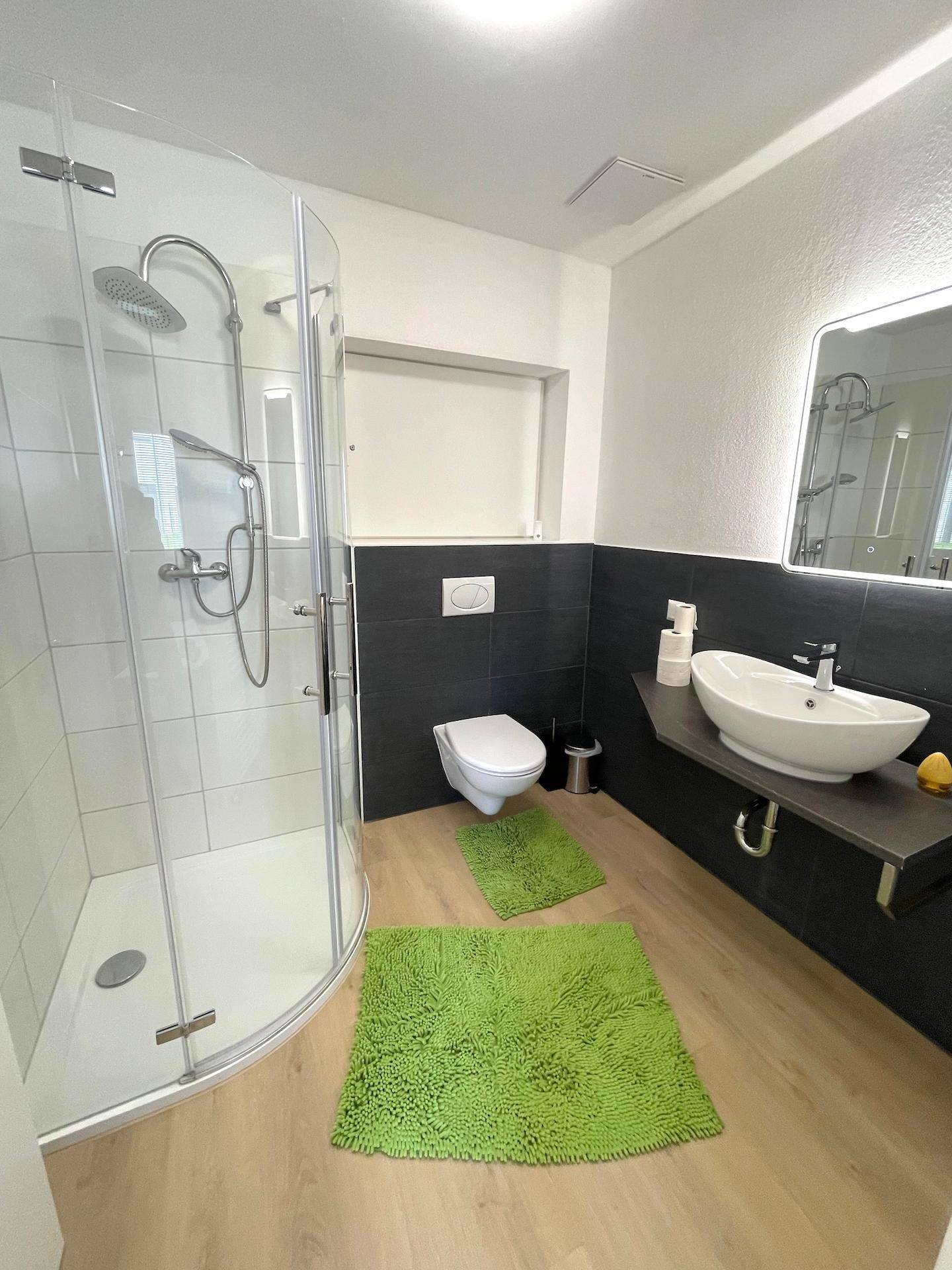 Ein modernes Badezimmer mit begehbarer Dusche, schwebendem Waschtisch und dunklen Akzentfliesen.