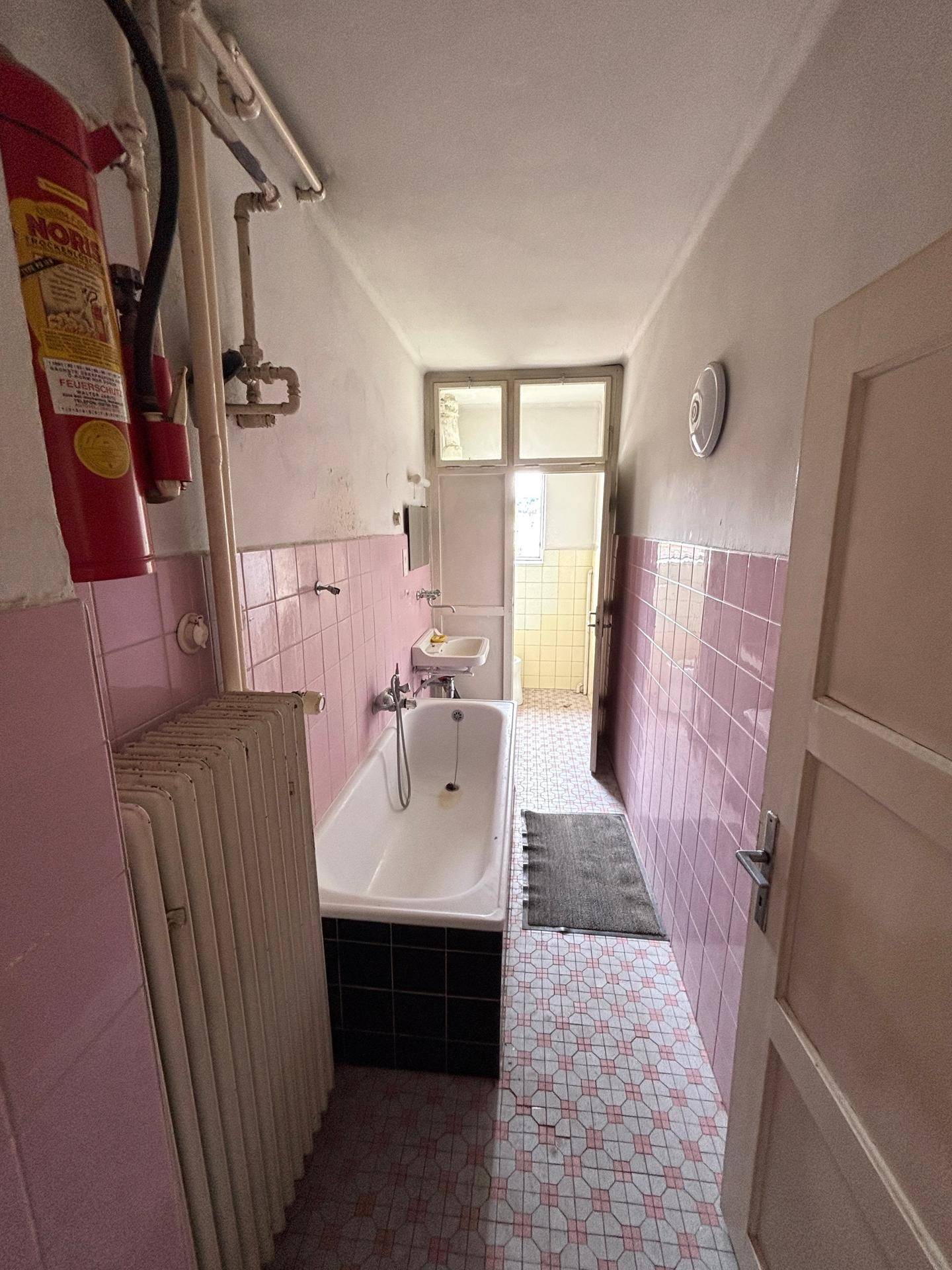 Langes Badezimmer mit rosa Fliesen, Badewanne und Heizkörper.