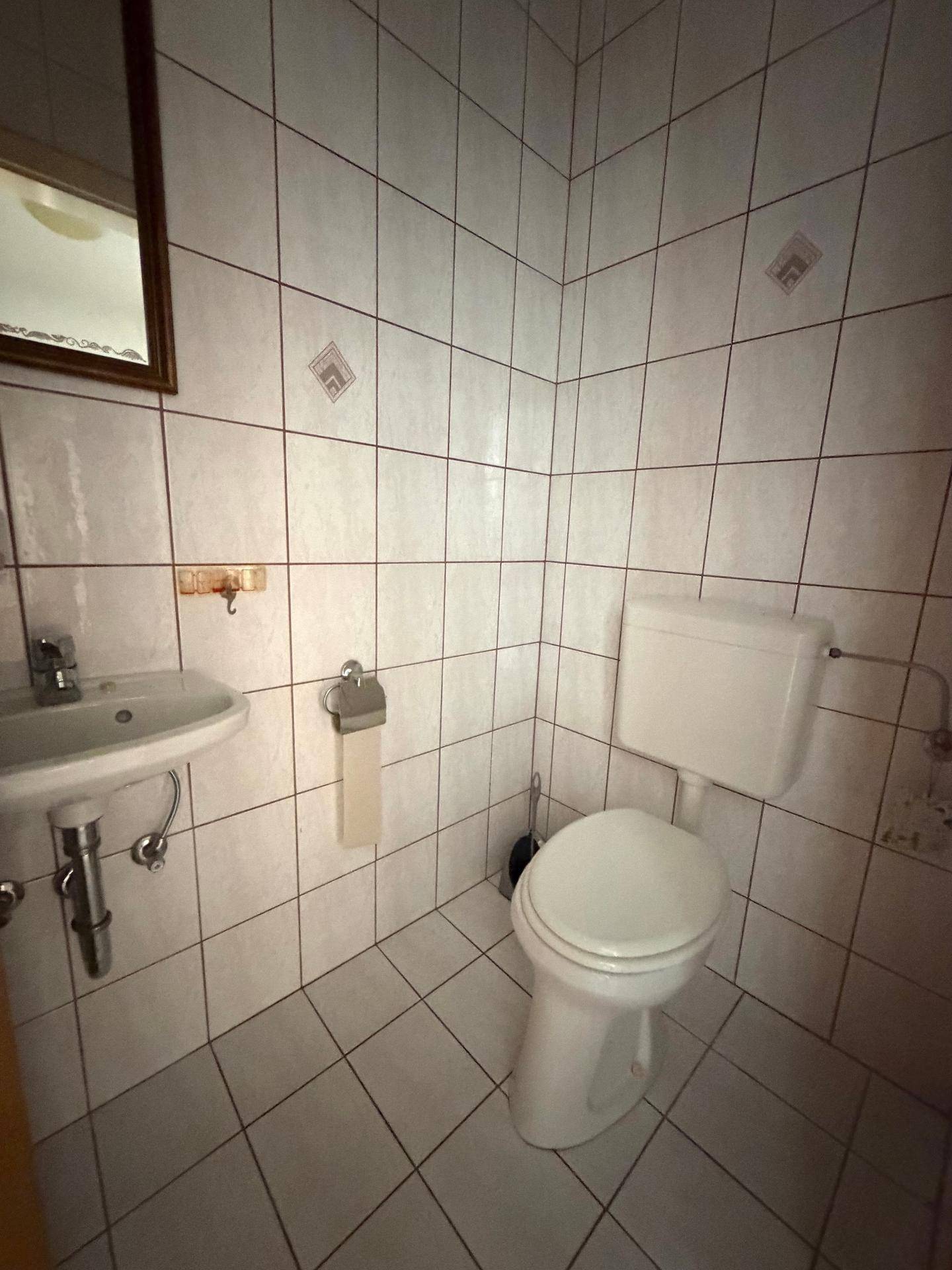 Kleines Gäste-WC mit Fliesenboden, Toilette und Handwaschbecken.