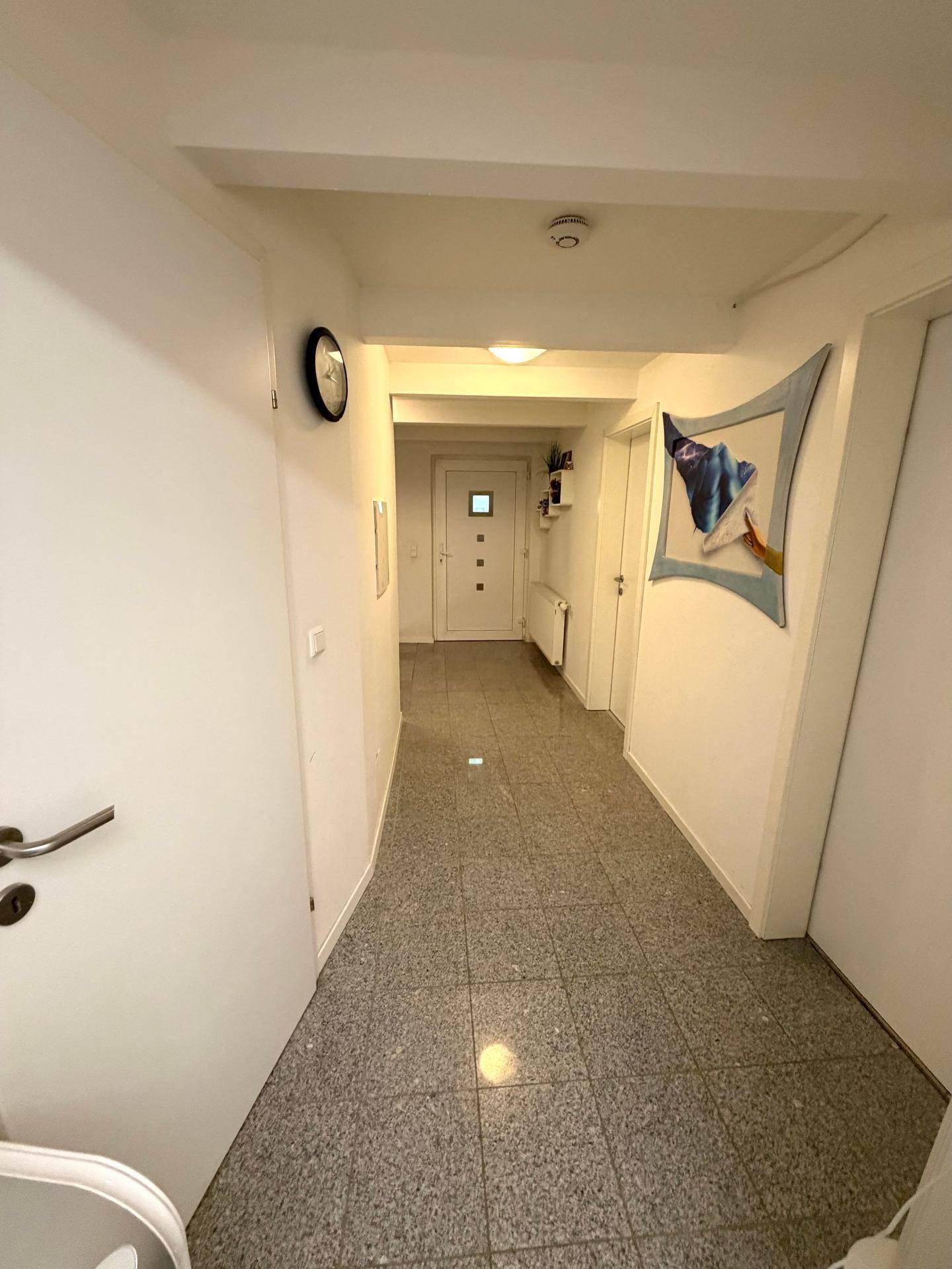 Langer Flur im Erdgeschoss mit Fliesenboden und weißer Eingangstür.