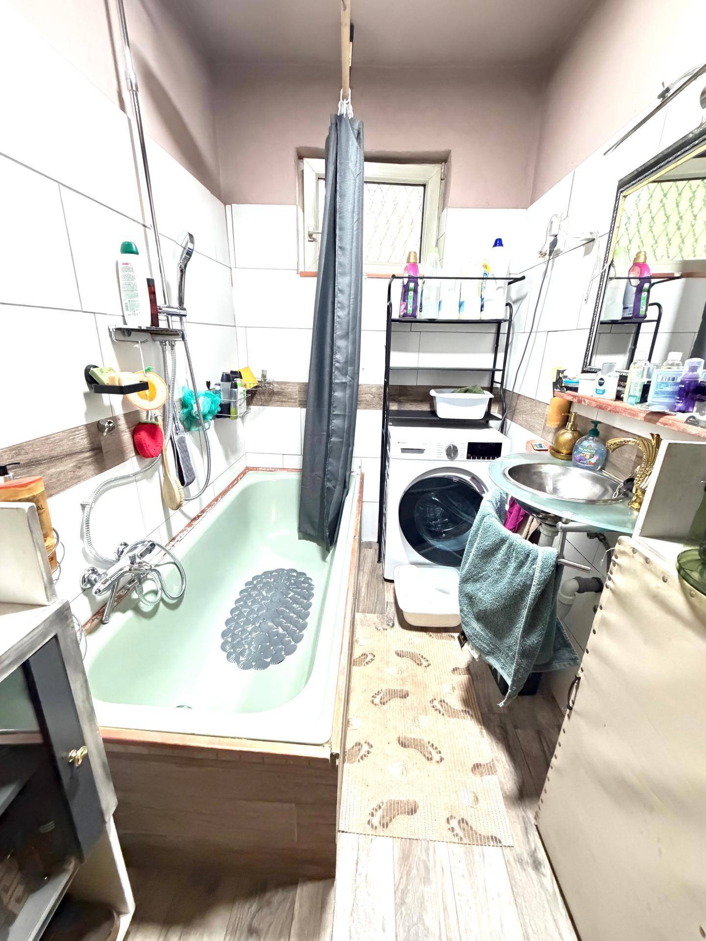 Badezimmer mit Badewanne, Waschbecken, Waschmaschine und Fenster für natürliche Belüftung.