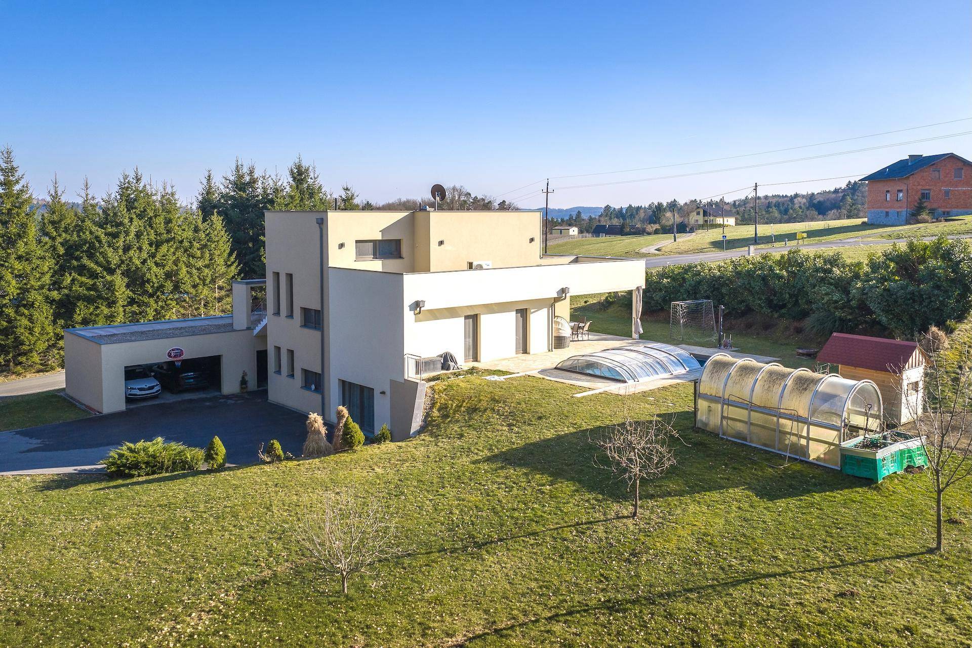 Panoramablick auf die moderne Villa mit Garage, Pool, Gewächshaus und weitläufigem Grundstück.