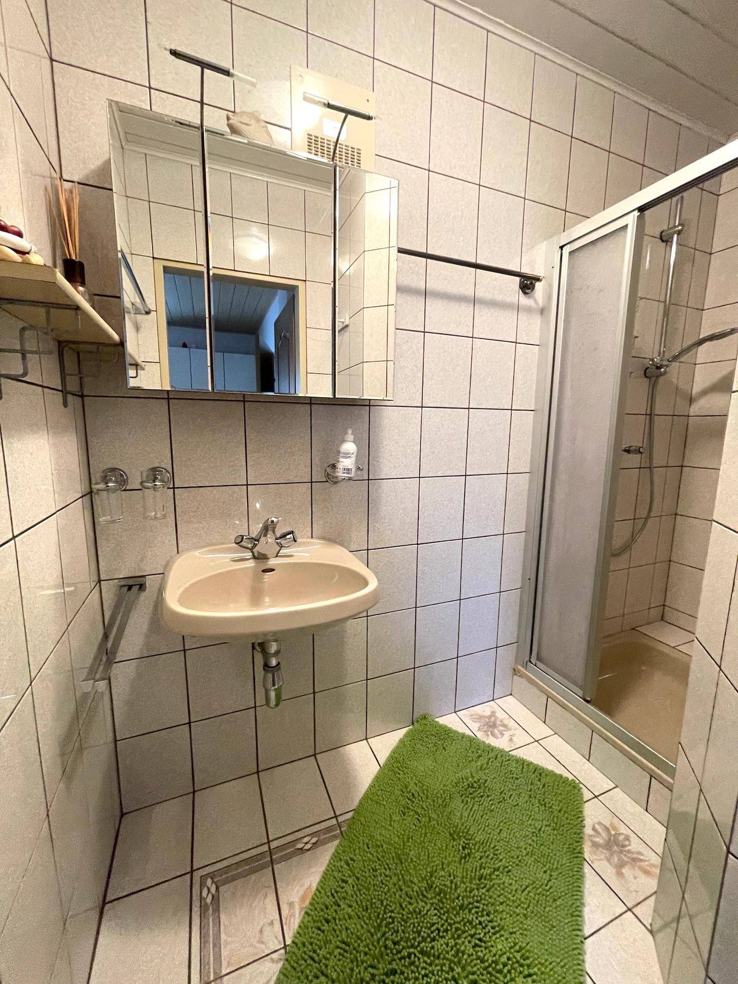 Ein Badezimmer mit hellen Fliesen, Waschbecken, Spiegelschrank und Duschkabine.