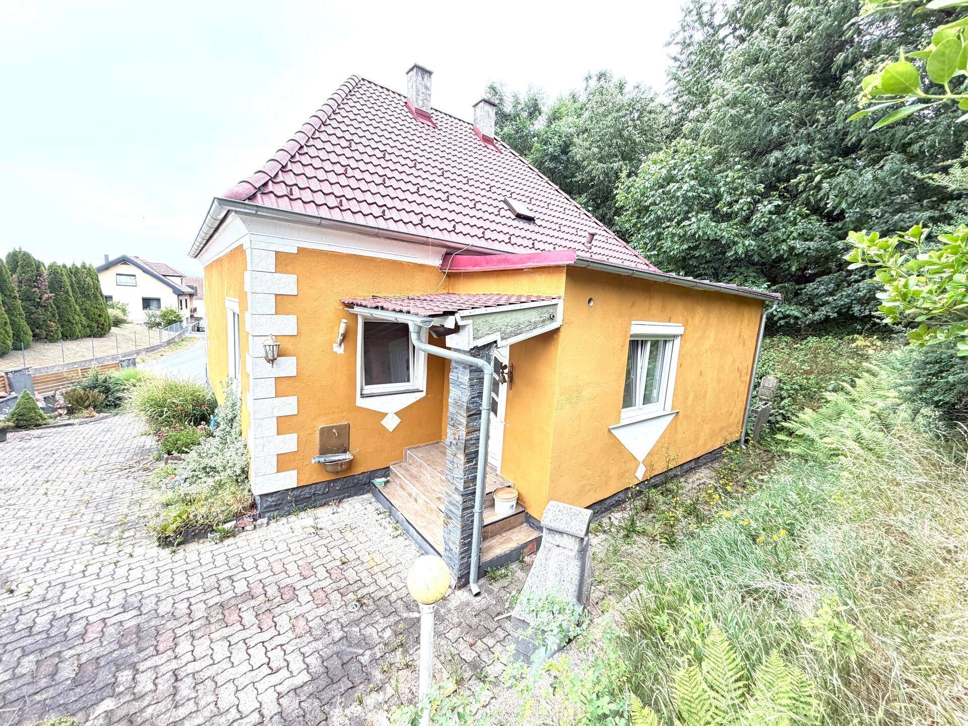 Hausansicht von oben mit gelber Fassade, rotem Ziegeldach und überdachtem Eingangsbereich.