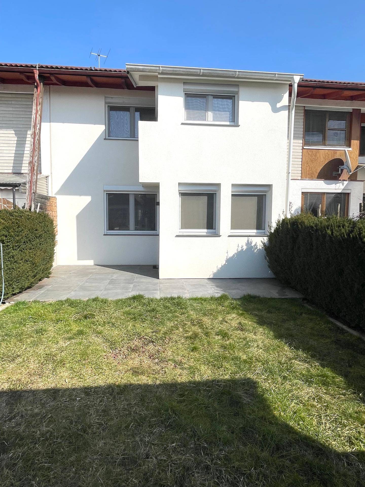 Rückansicht des Hauses mit Garten, Terrasse und weißer Fassade.