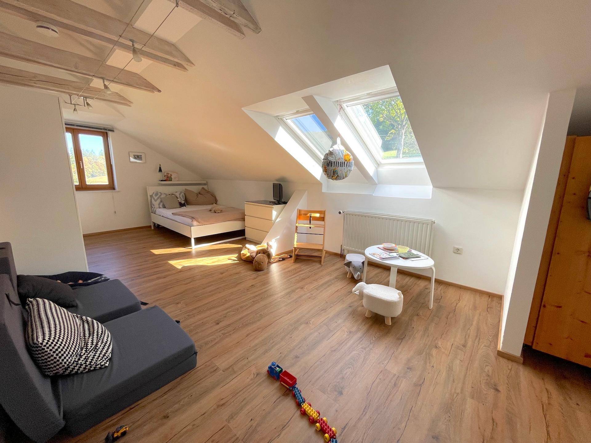 Freundliches Kinderzimmer im Dachgeschoss mit Dachfenstern, Holzboden und einem gemütlichen Spielbereich.