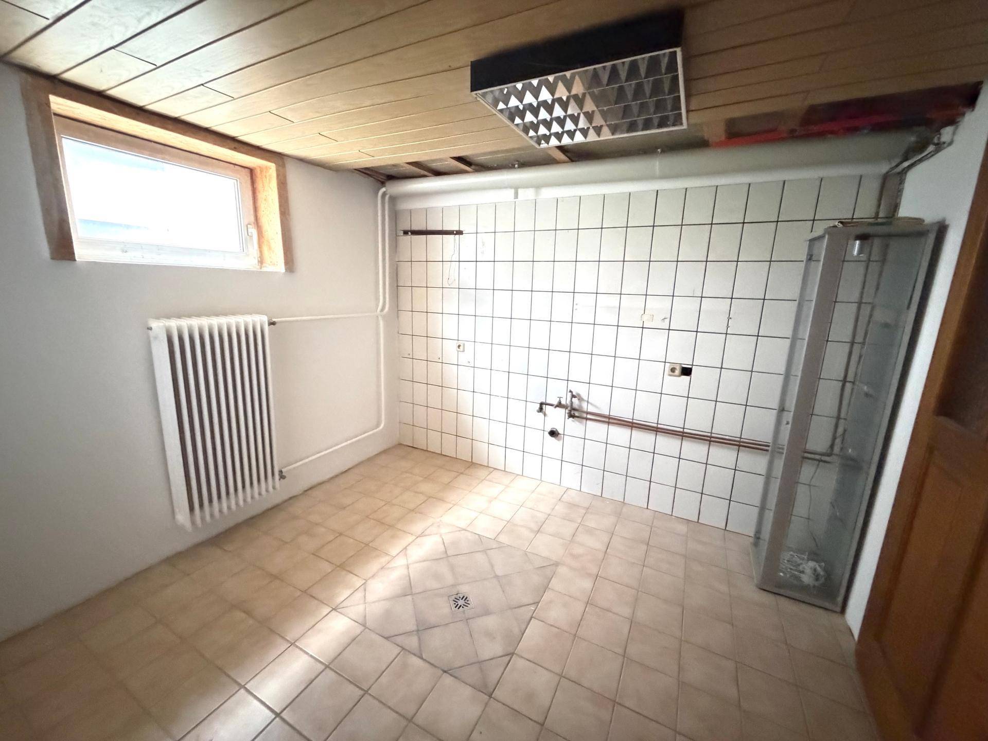 Funktionaler Hauswirtschaftsraum mit Fliesenboden, Heizkörper und Fenster für Belüftung.