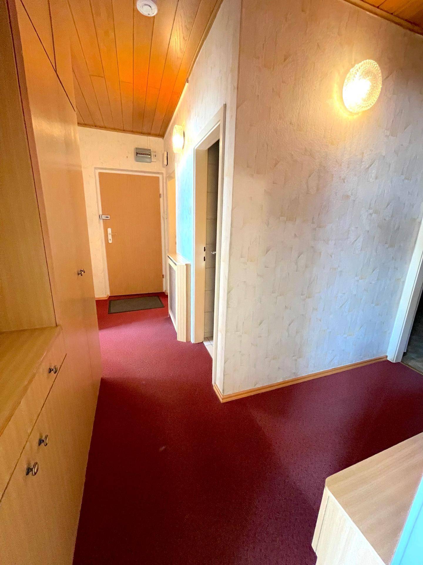 Flur mit rotem Teppichboden, Holzverkleidung an der Decke und Einbauschränken.
