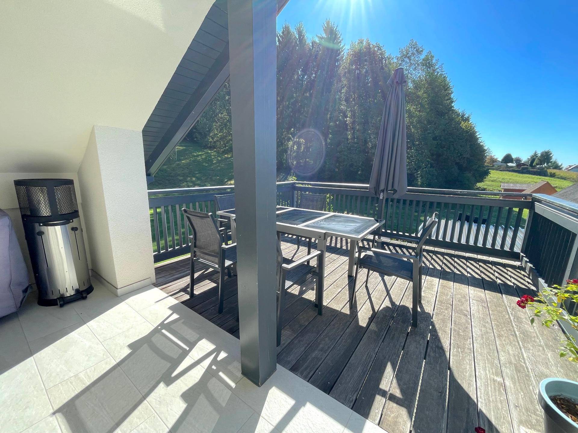 Sonnige Terrasse mit Holzboden, Gartenmöbeln und weitem Blick auf die umliegende Natur.