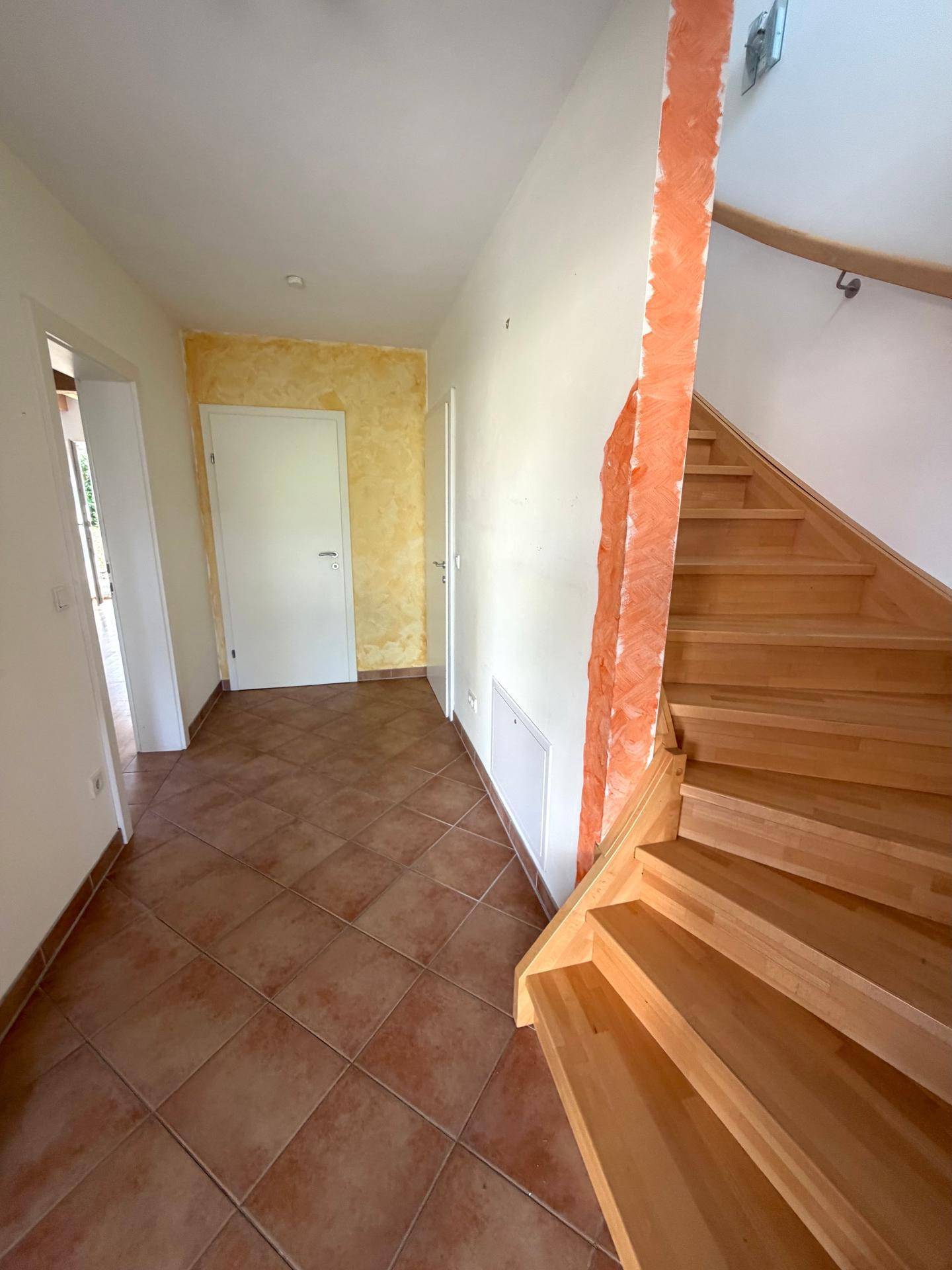 Heller Flur mit Terrakottafliesen und Holztreppe, die in die oberen Etagen führt.