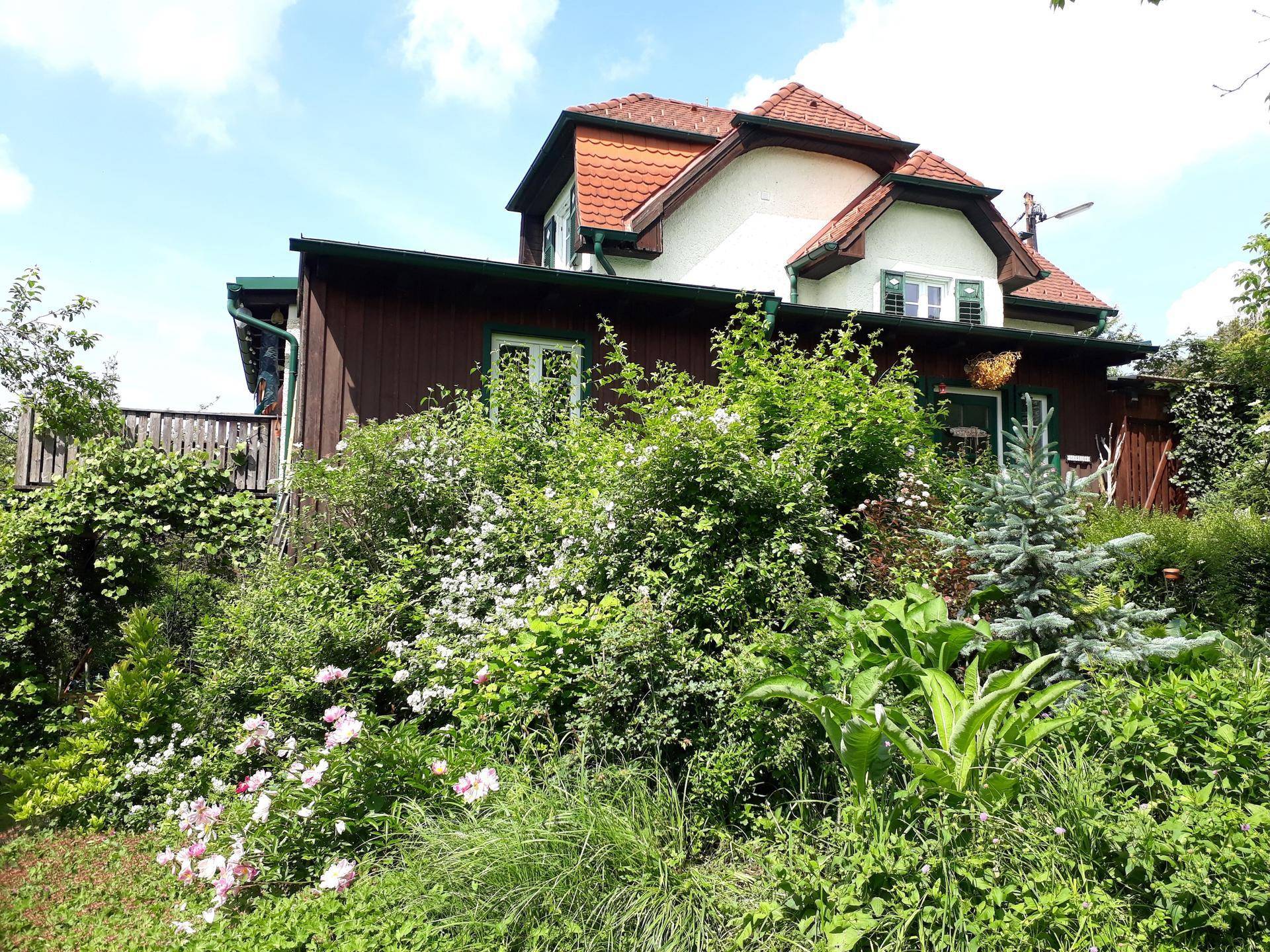 Malerisches Landhaus mit traditionellem Dach und üppiger Bepflanzung im Vorgartenbereich.