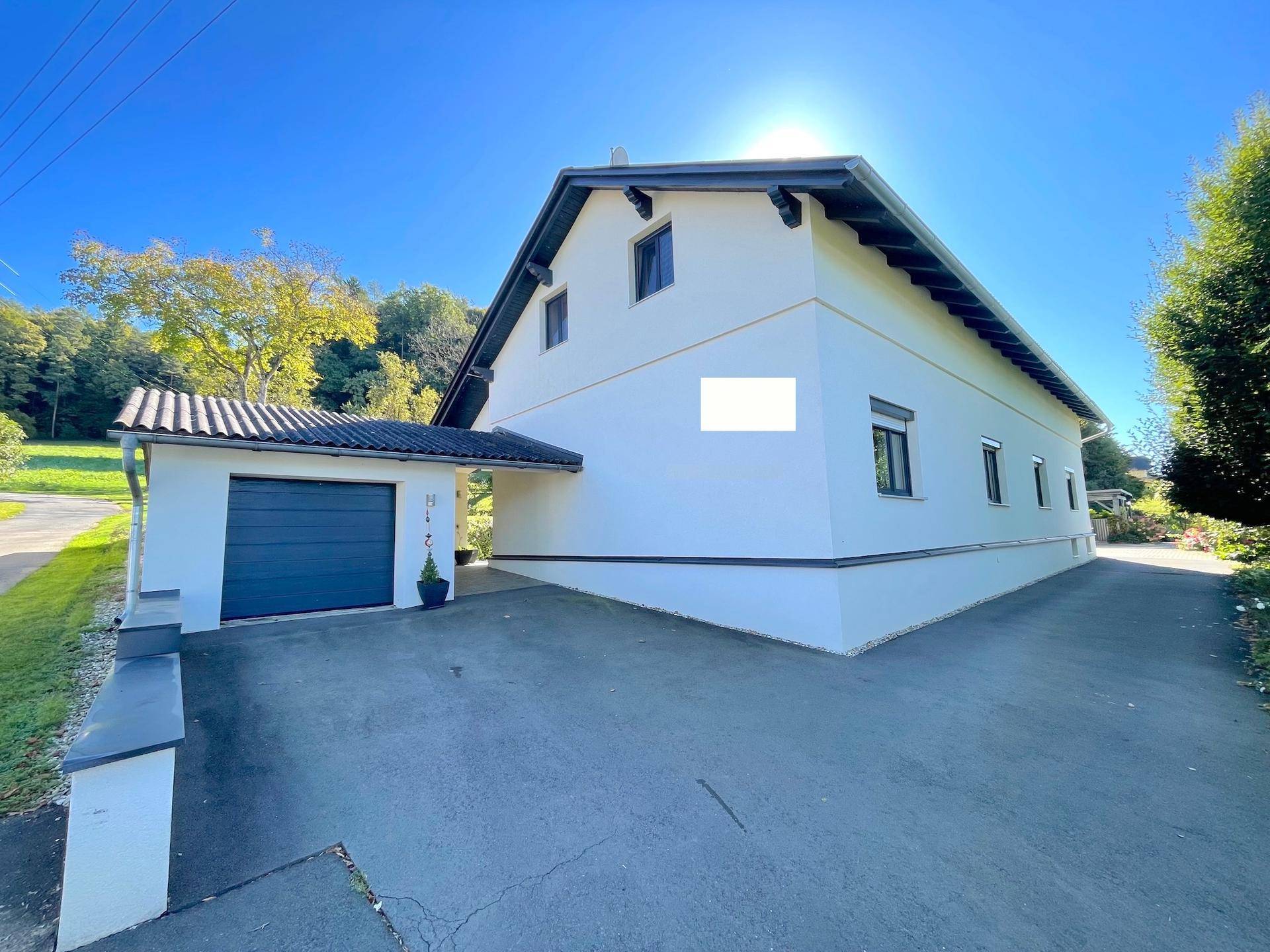 Seitenansicht des Hauses mit integrierter Garage und breiter Zufahrt unter blauem Himmel.