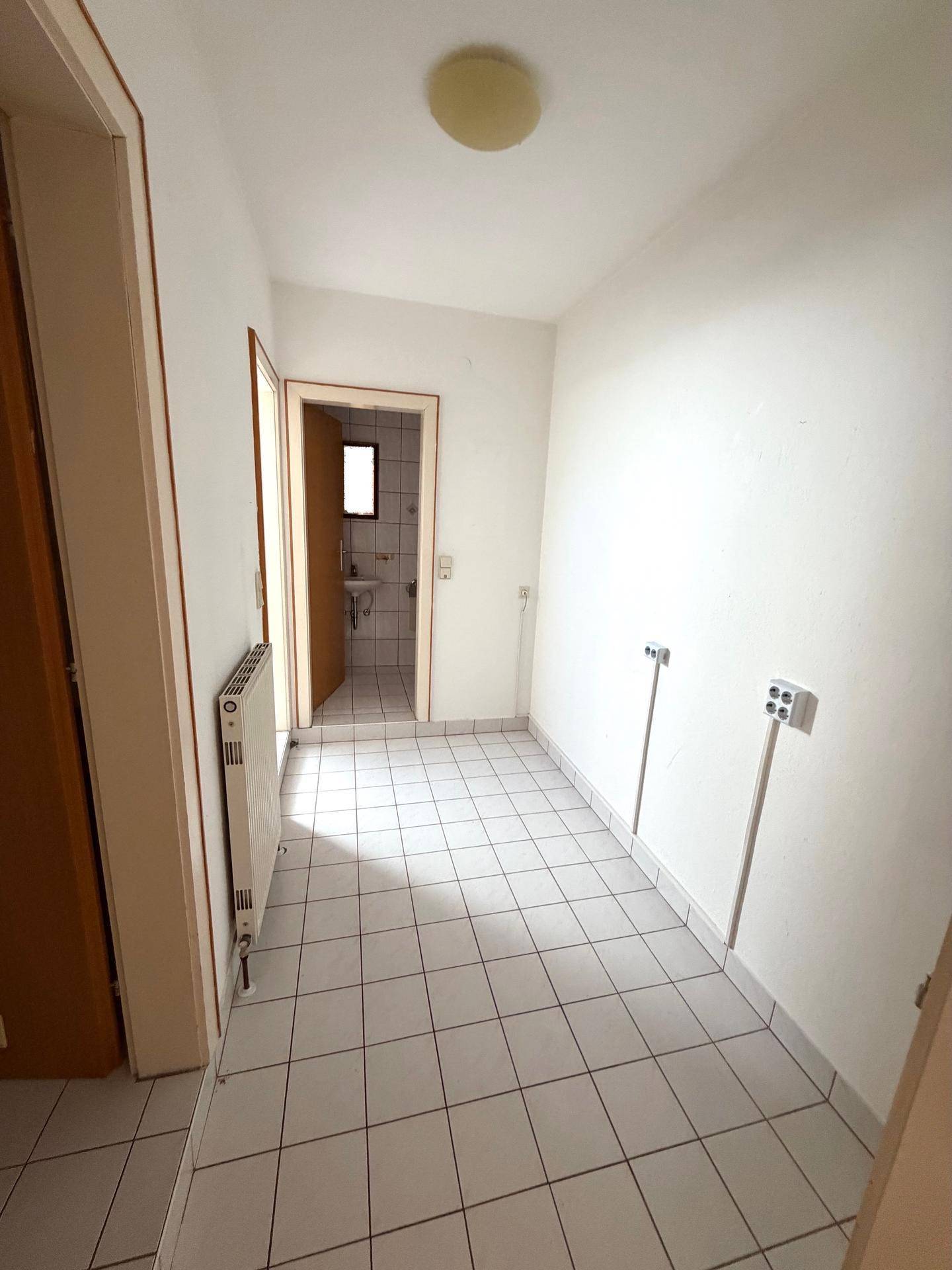 Praktischer Hauswirtschaftsraum mit Fliesenboden, Heizkörper und Zugang zum Badezimmer.