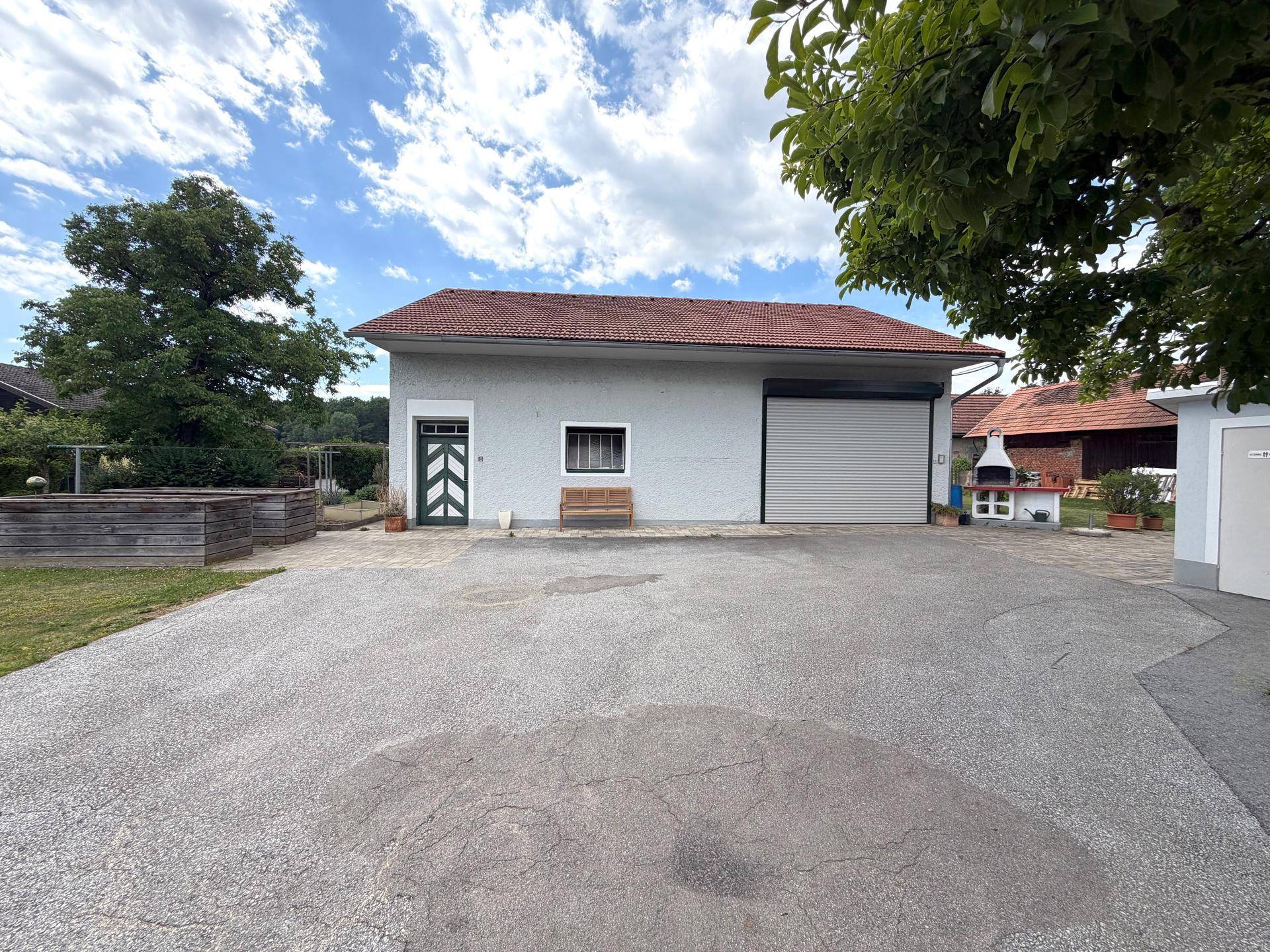Vorderansicht des Gebäudes mit großer Garage, gepflasterter Zufahrt und seitlichem Grillbereich.