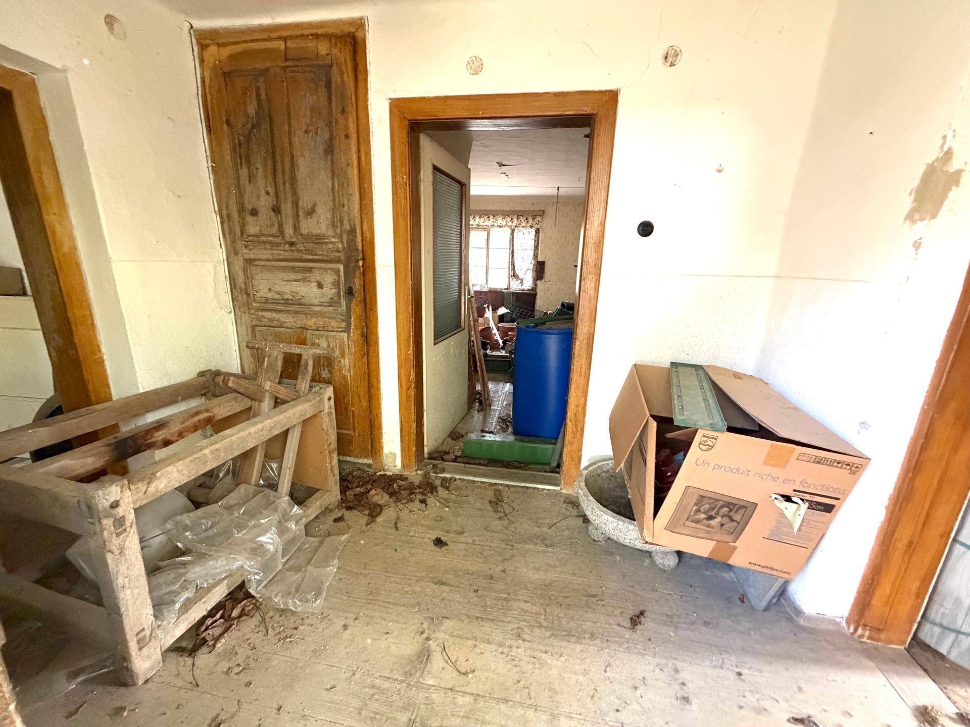 Flur mit alten Holztüren und Blick in einen weiteren Raum des renovierungsbedürftigen Hauses.