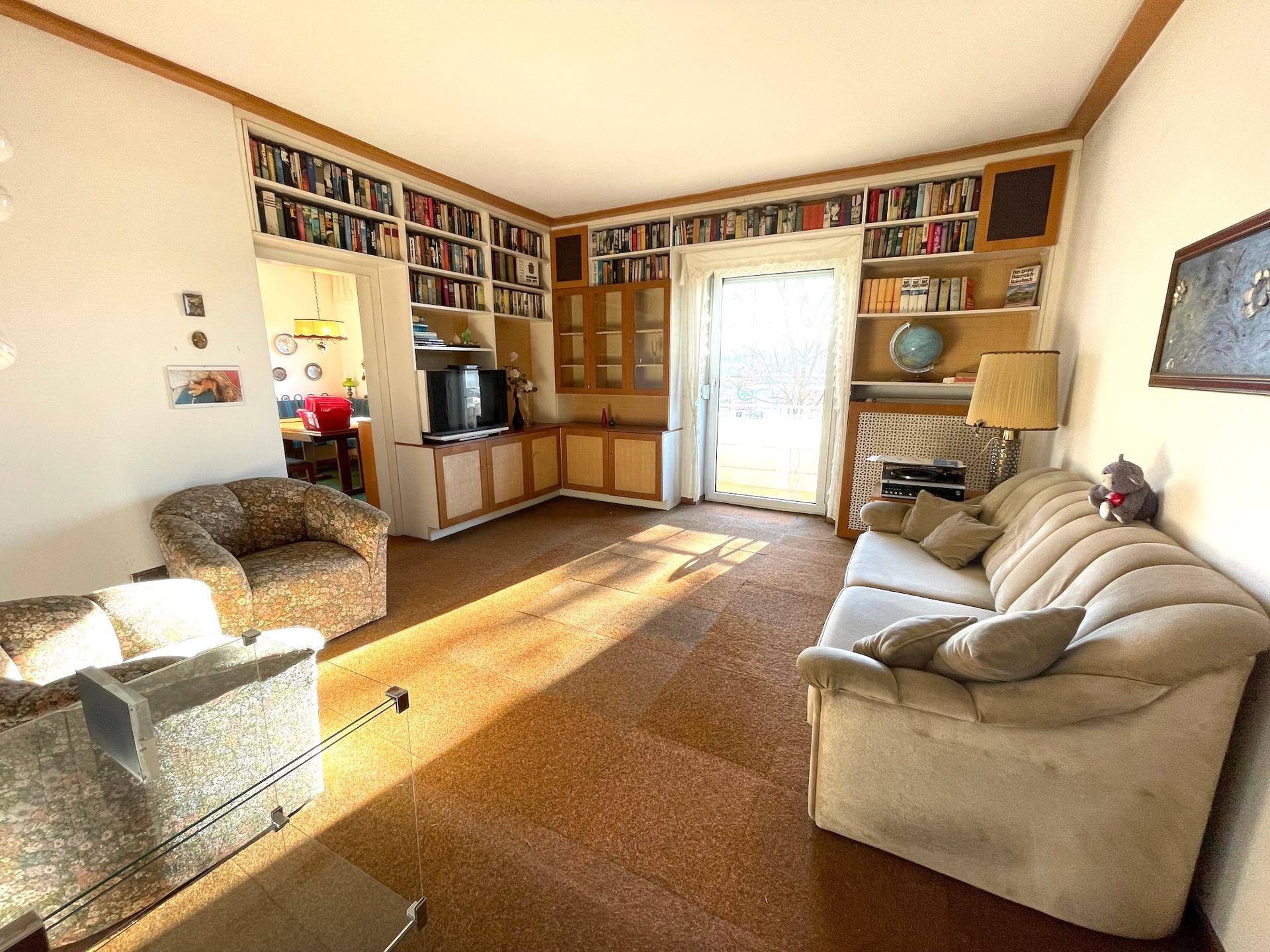 Geräumiges Wohnzimmer mit Teppichboden, Bücherregalen und viel Tageslicht.