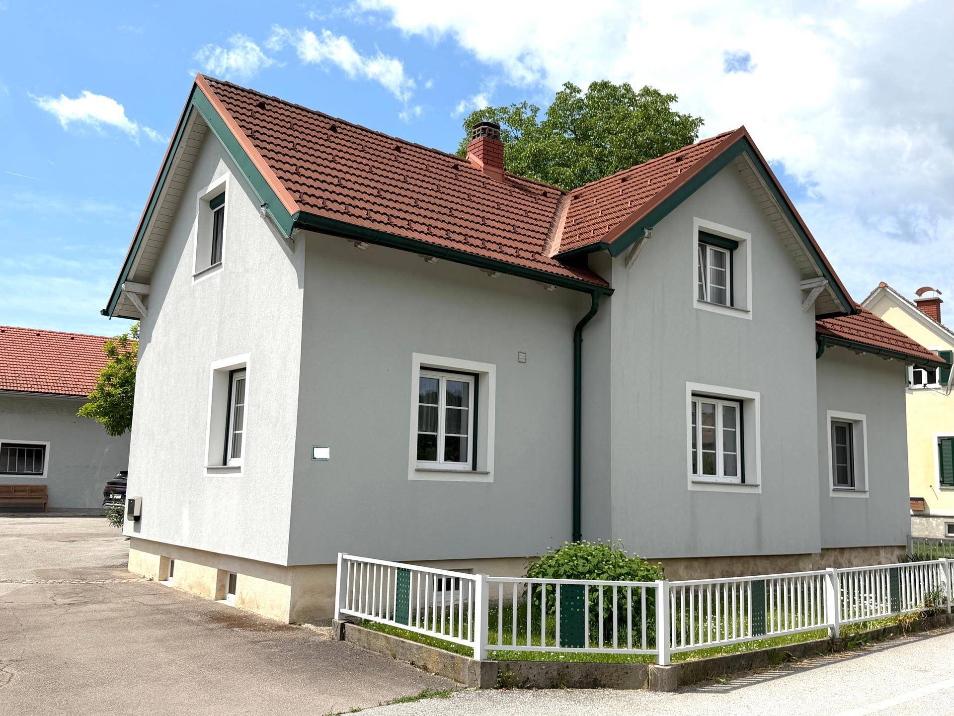 Gepflegtes Wohnhaus mit heller Fassade, roten Dachziegeln und umgebendem Gartenbereich.