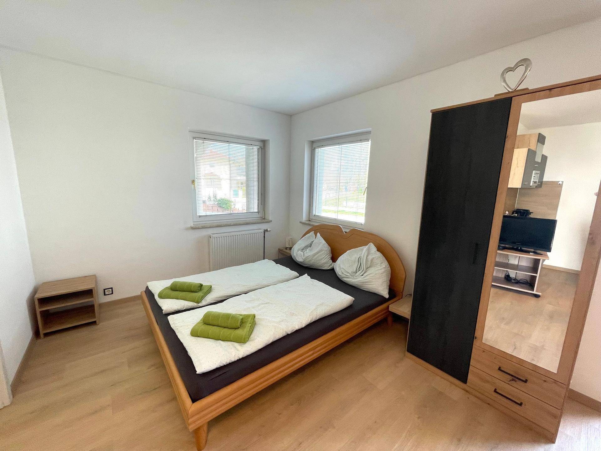 Ein helles Schlafzimmer mit Doppelbett, Laminatboden und Spiegelschrank.