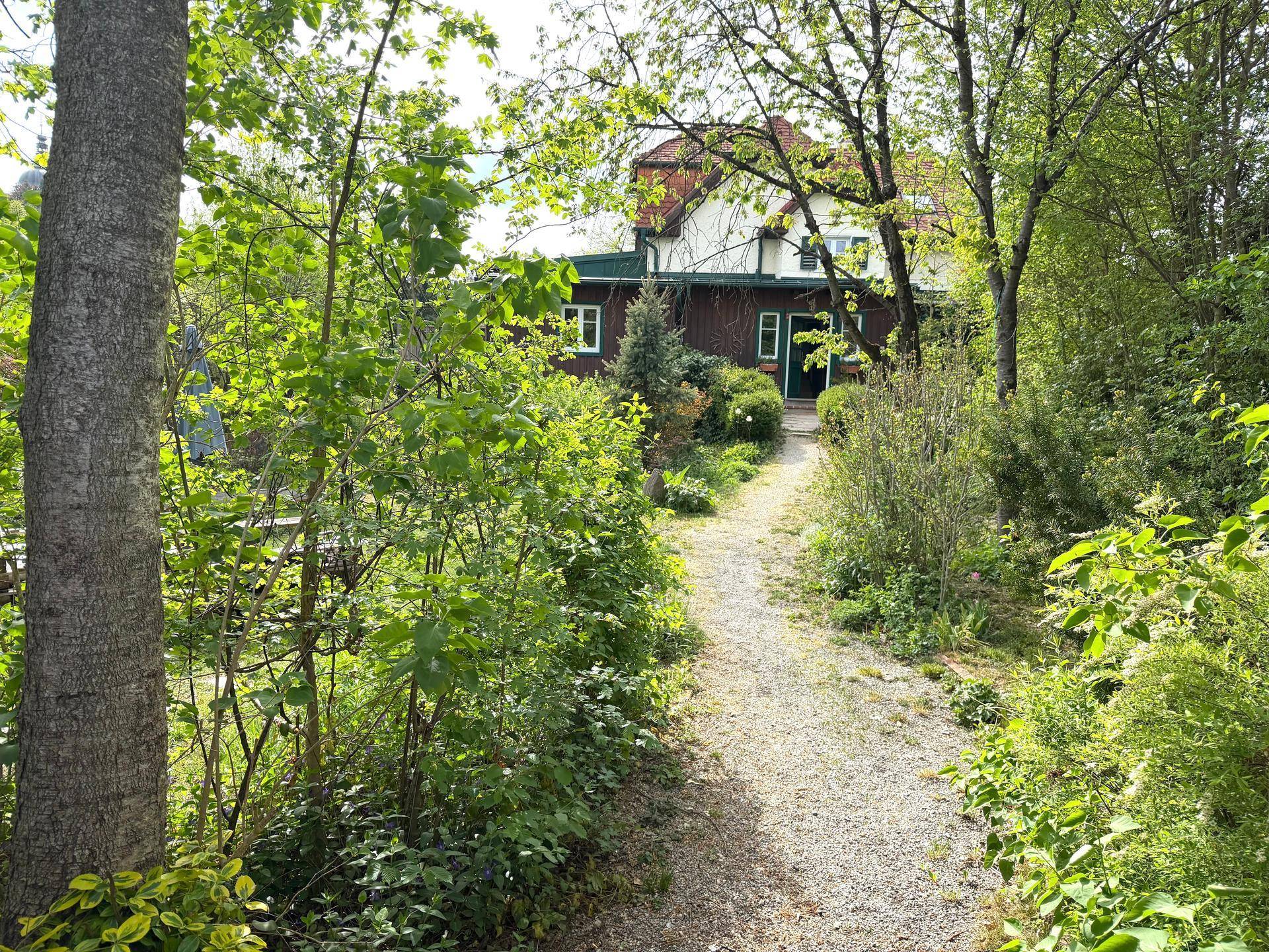 Hausansicht mit langem Gartenweg, umgeben von üppigem Grün und Bäumen.