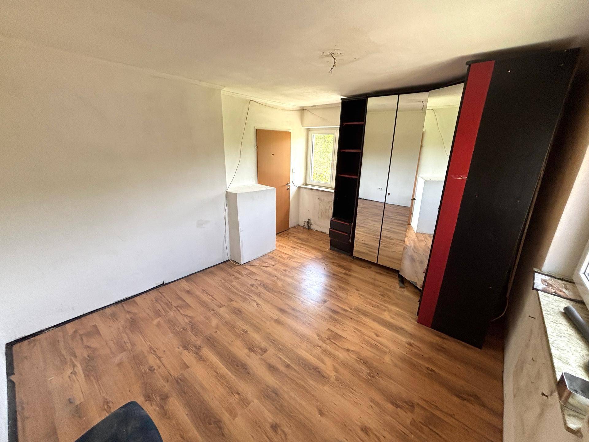 Weiterer Blick in das helle Zimmer mit Laminatboden und großem Spiegelschrank.