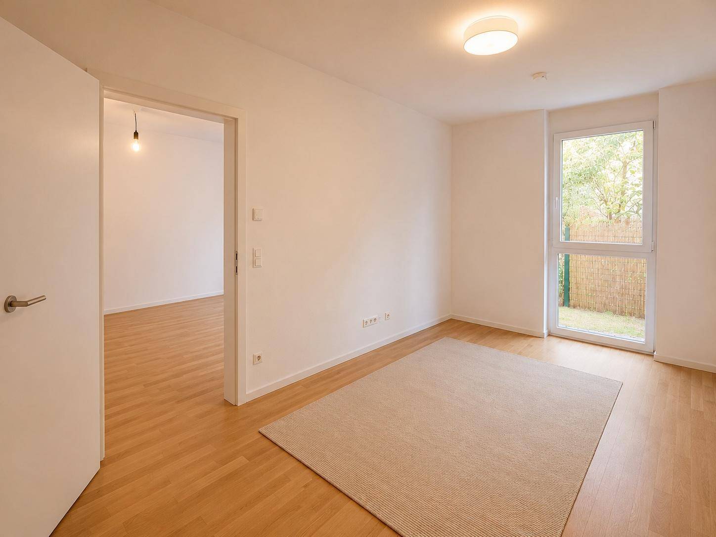 Helles Zimmer mit Holzfußboden, großem Fenster und Zugang zu einem kleinen Außenbereich, bereit zur Einrichtung.