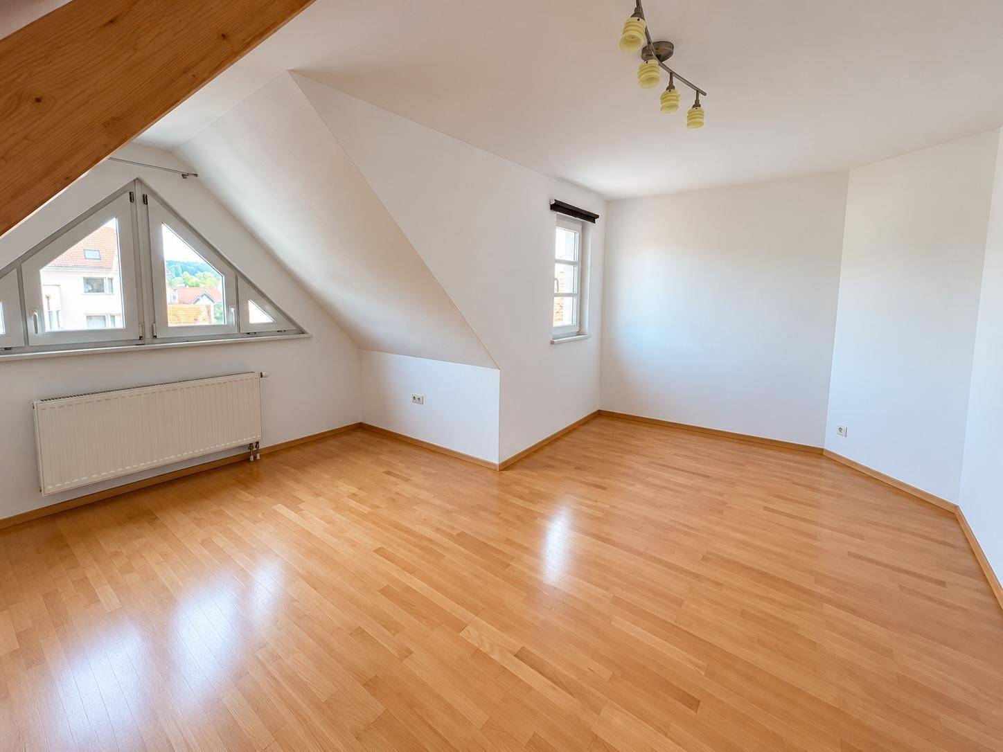 Helles Dachgeschosszimmer mit Parkettboden, Schrägen und mehreren Fenstern für viel Tageslicht.