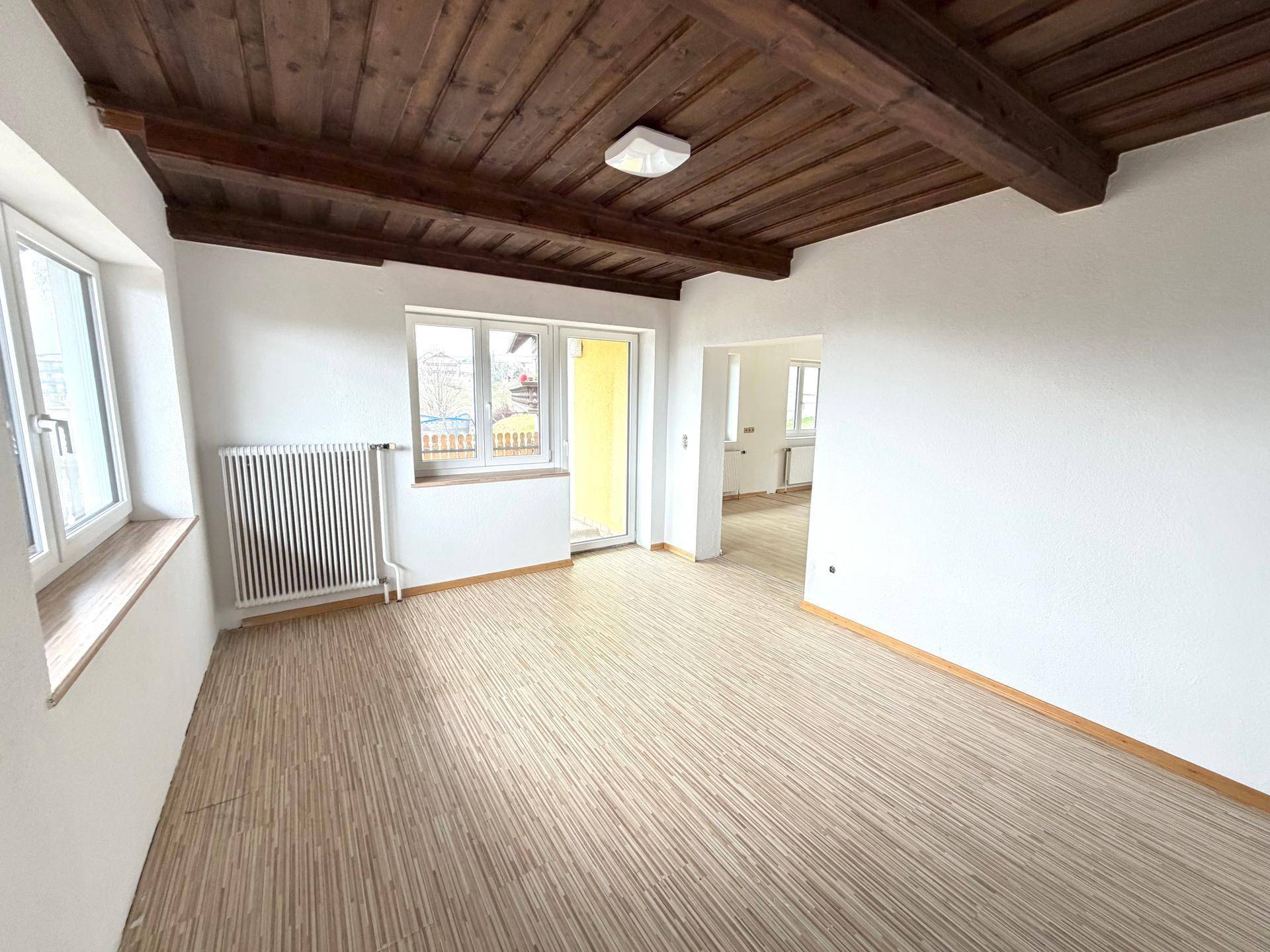 Heller Wohnraum mit Holzbalkendecke, Laminatboden und Zugang zu einem Balkon mit schöner Aussicht.