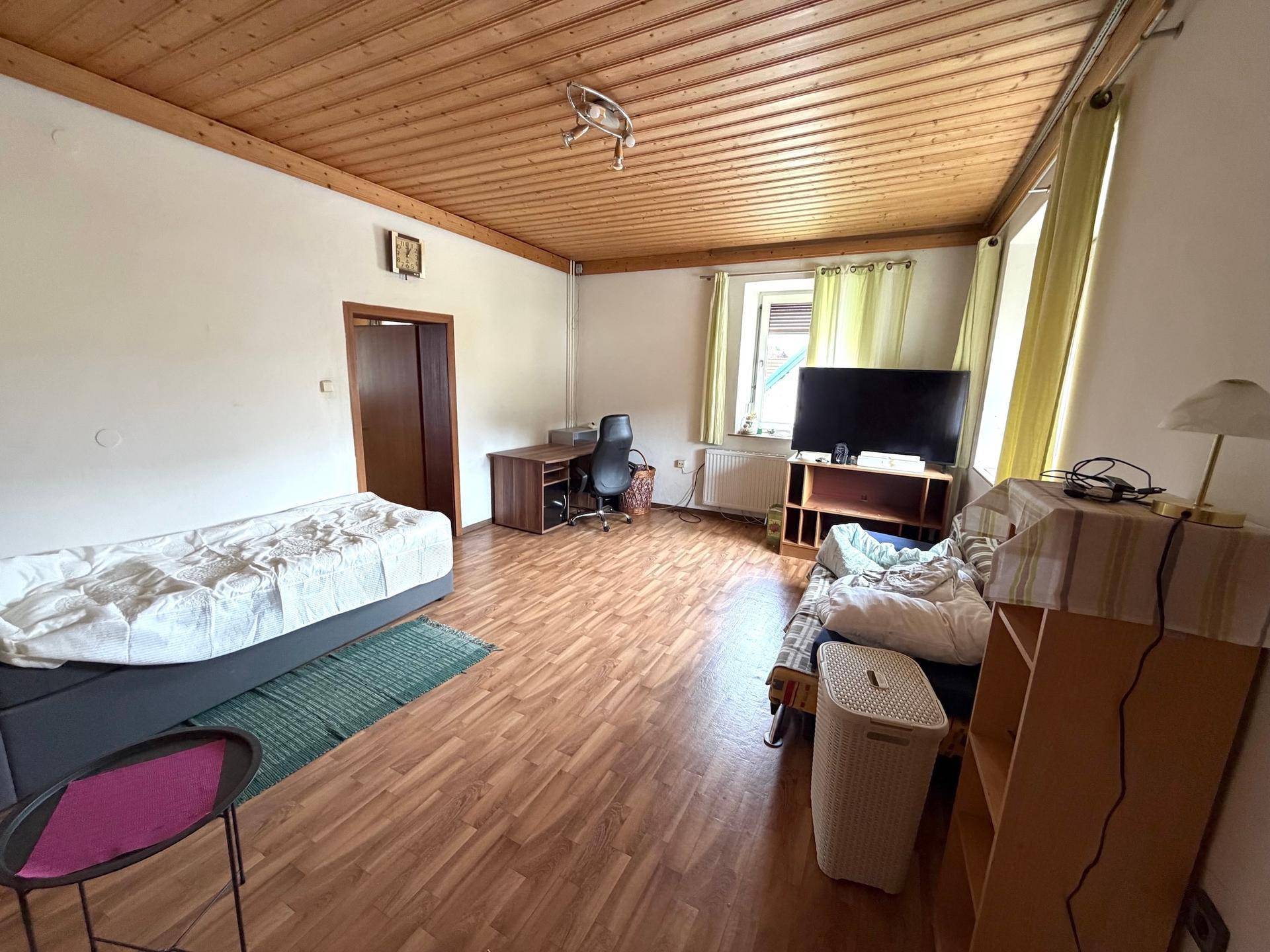 Helles Schlafzimmer mit Laminatboden, Holzdecke und Schreibtischbereich.