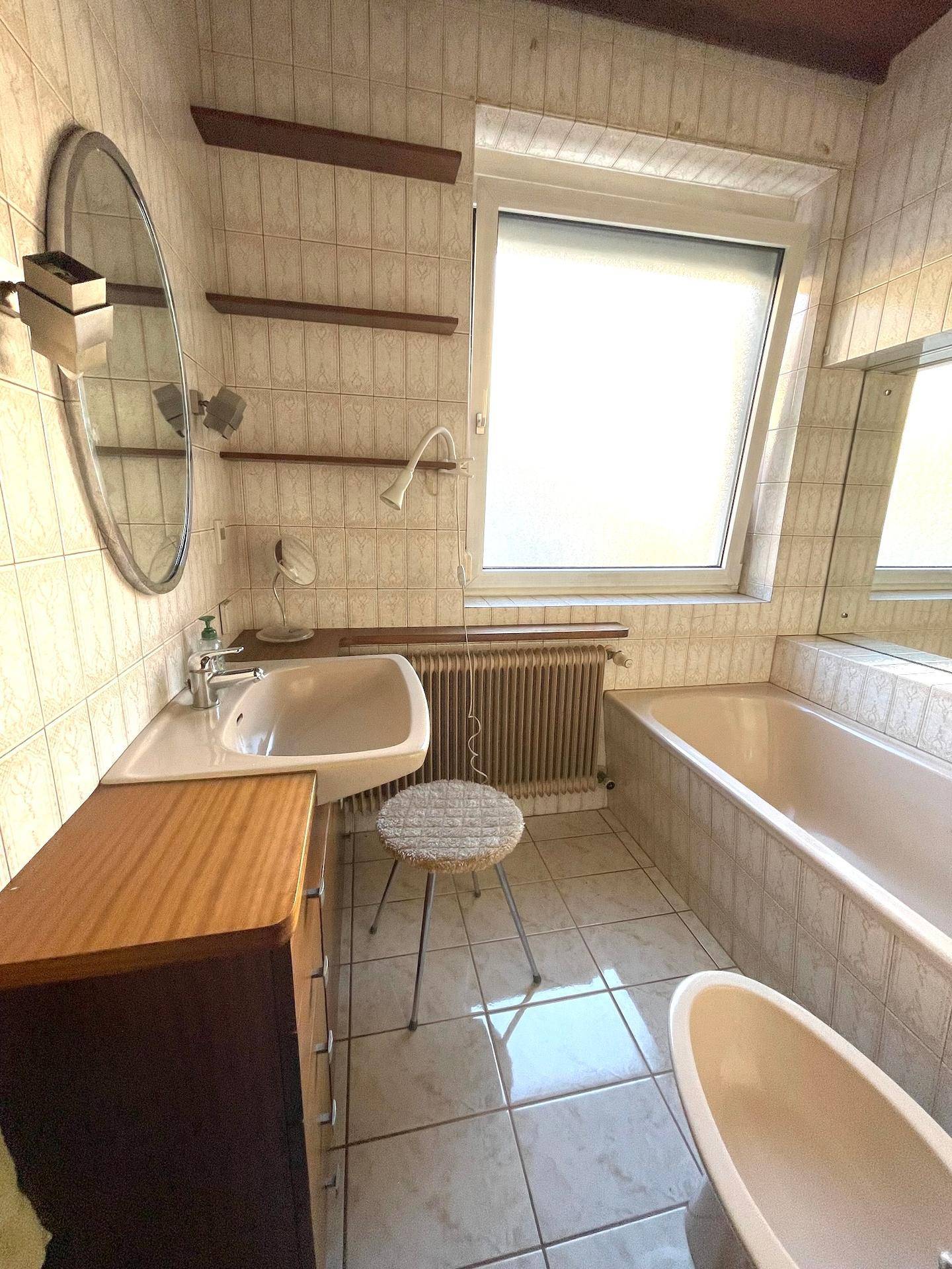 Helles Badezimmer mit Badewanne, Waschbecken und Fenster für Tageslicht.