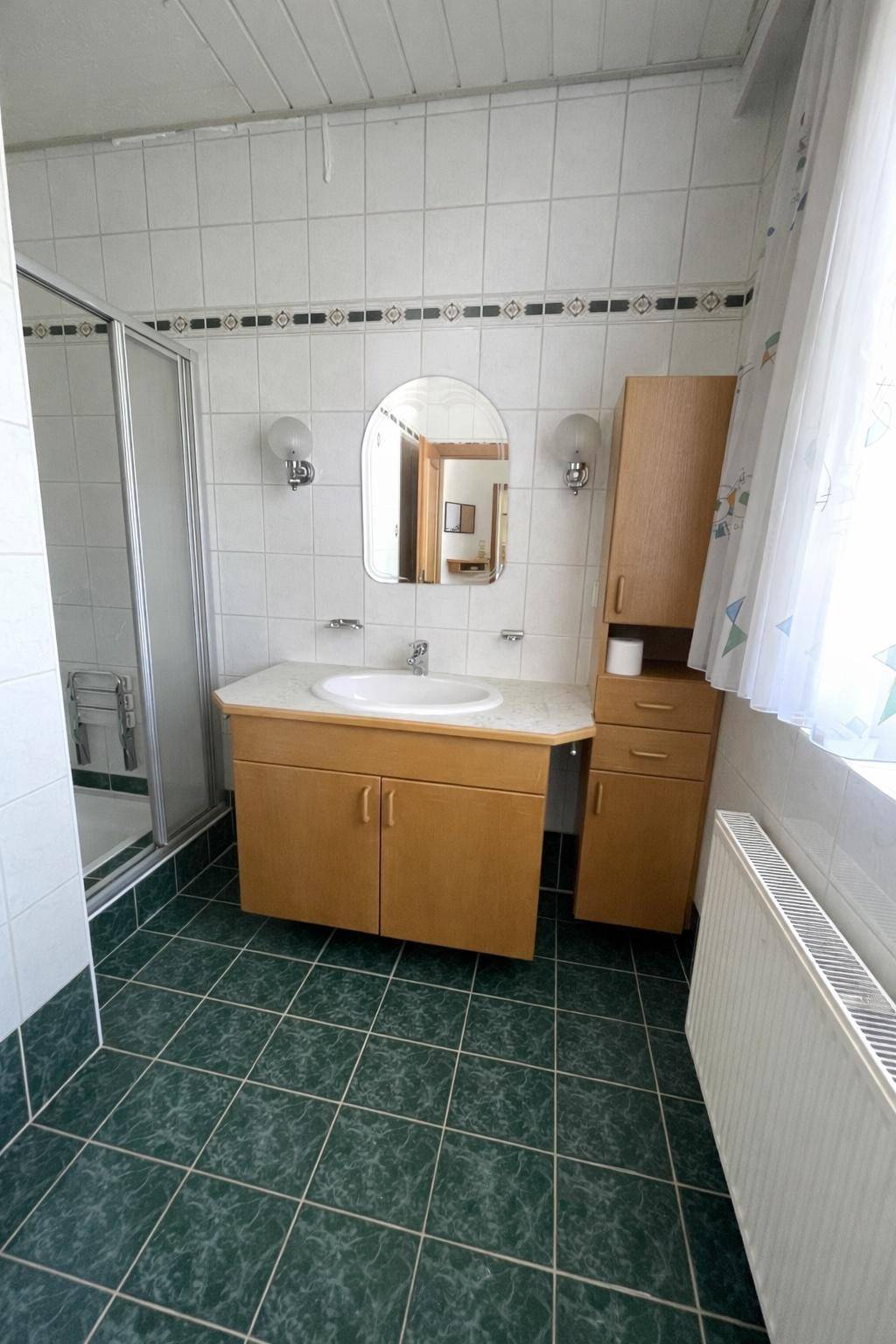 Badezimmer mit Duschkabine, Waschbecken und grünen Fliesen.