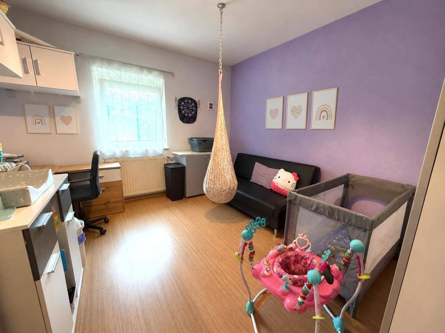 Kinderzimmer mit Wickeltisch, Babybett und Schreibtisch, in freundlichen Farben gestaltet.