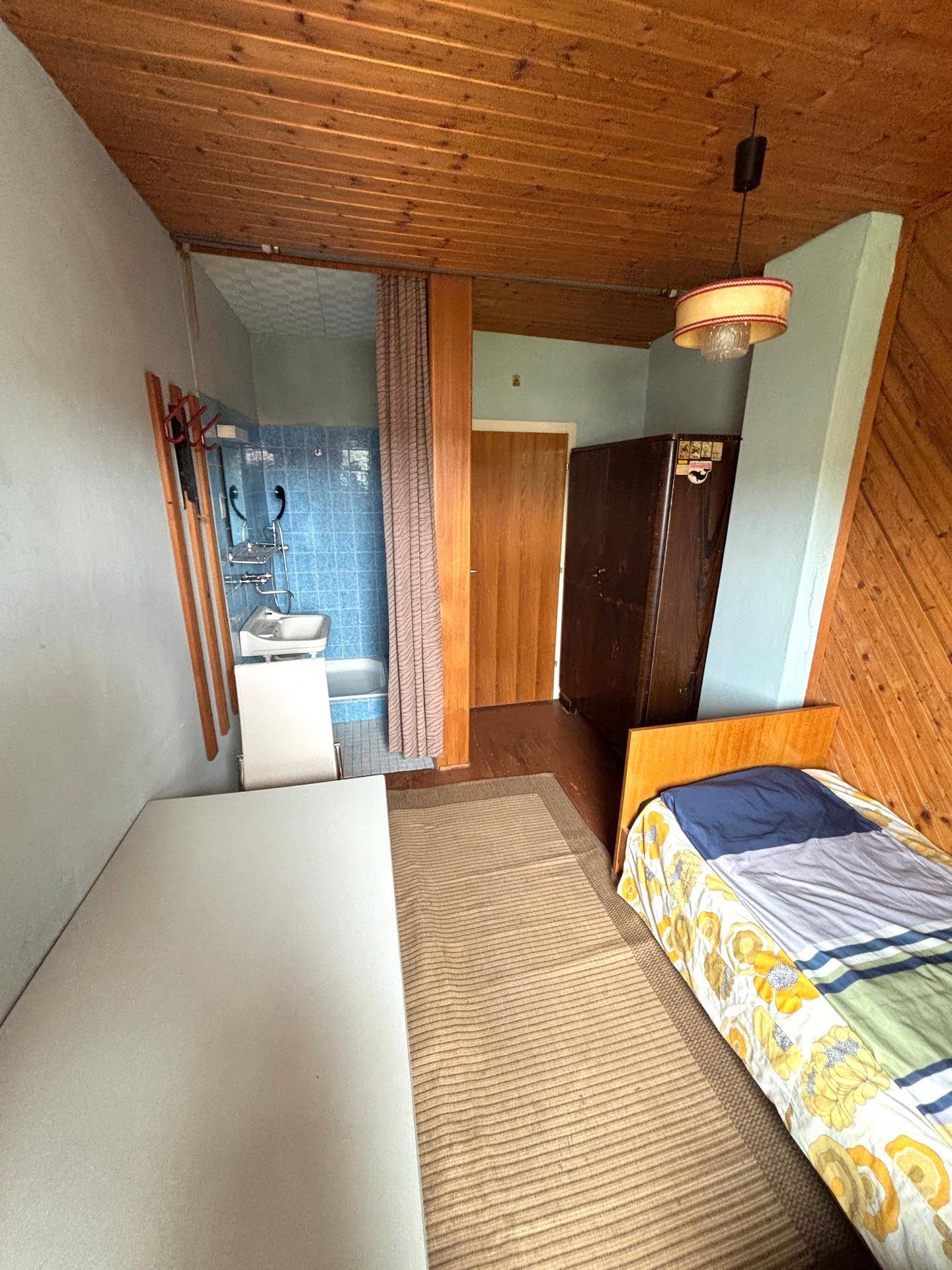 Schlafzimmer mit Holzwänden und integriertem Waschbereich mit blauen Fliesen.
