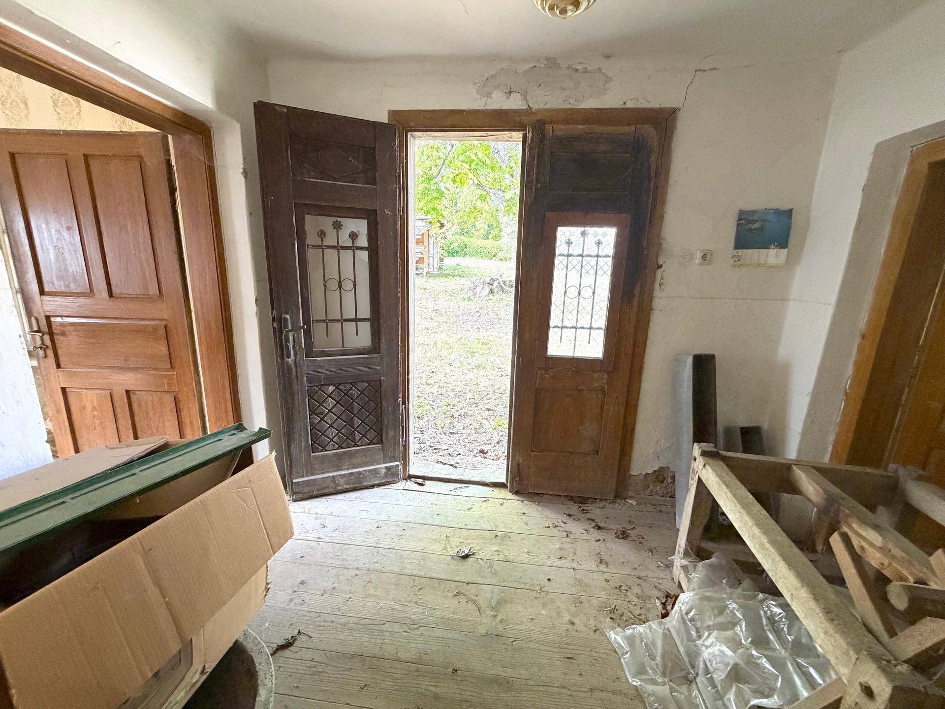 Eingangsbereich eines alten Hauses mit Holztüren und Blick in den verwilderten Garten.