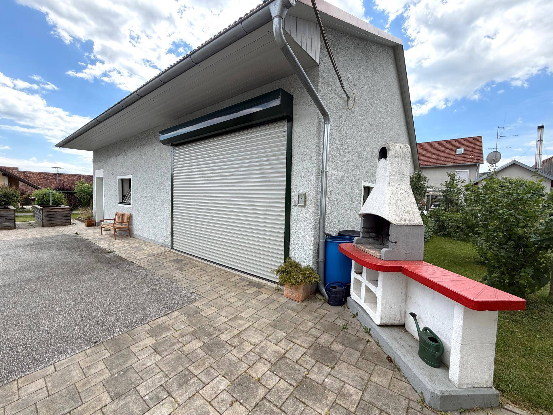 Außenbereich mit großer Garage, gepflastertem Vorplatz und gemauertem Grillplatz für gesellige Stunden.