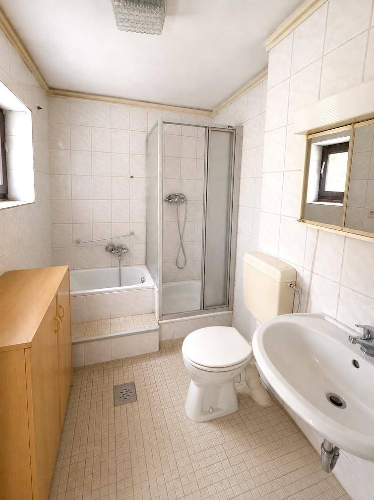 Helles Badezimmer mit Badewanne, Dusche, WC und Waschbecken, komplett gefliest.