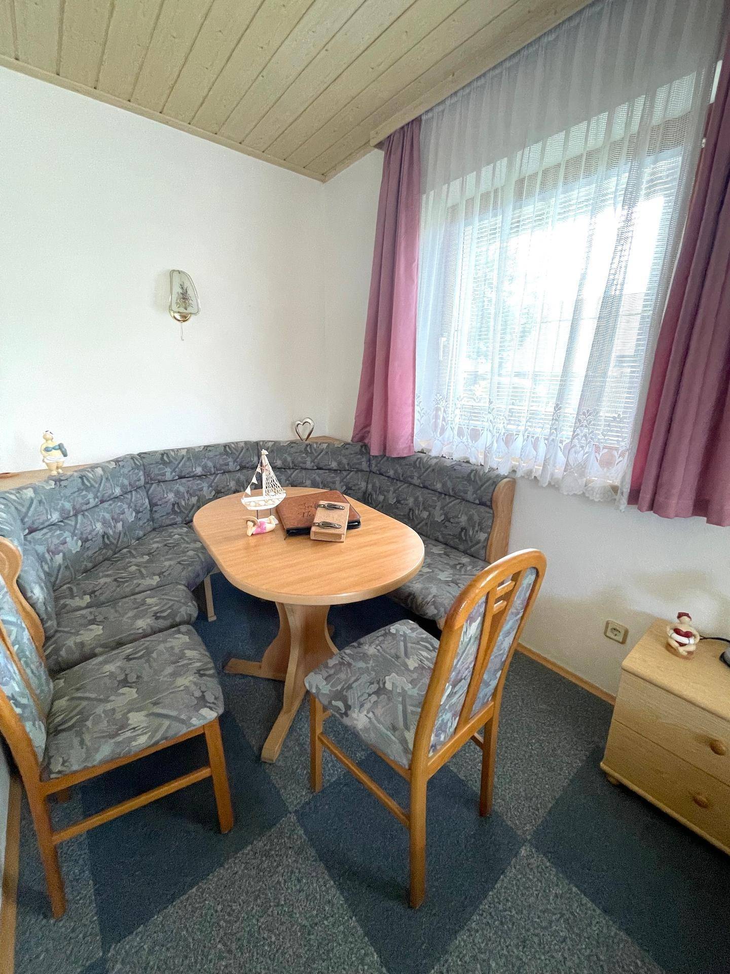 Eine traditionelle Essecke mit Eckbank, Holztisch und Teppichboden unter einer Holzdecke.