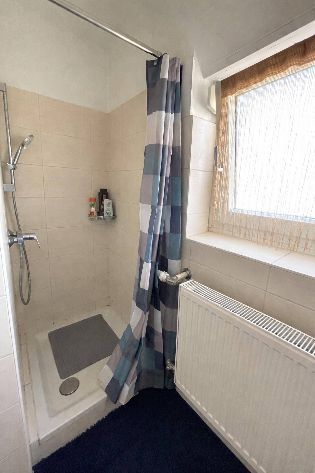Badezimmer mit Duschkabine, Fenster und hellen Fliesen.