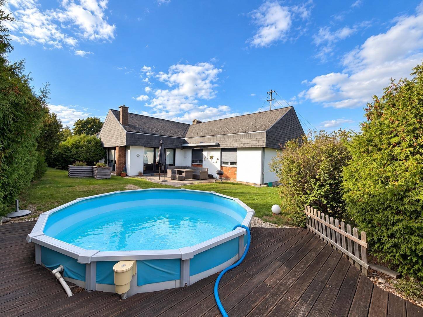 Hinterhof mit großem Holzdeck, Aufstellpool und Terrasse mit Gartenmöbeln.