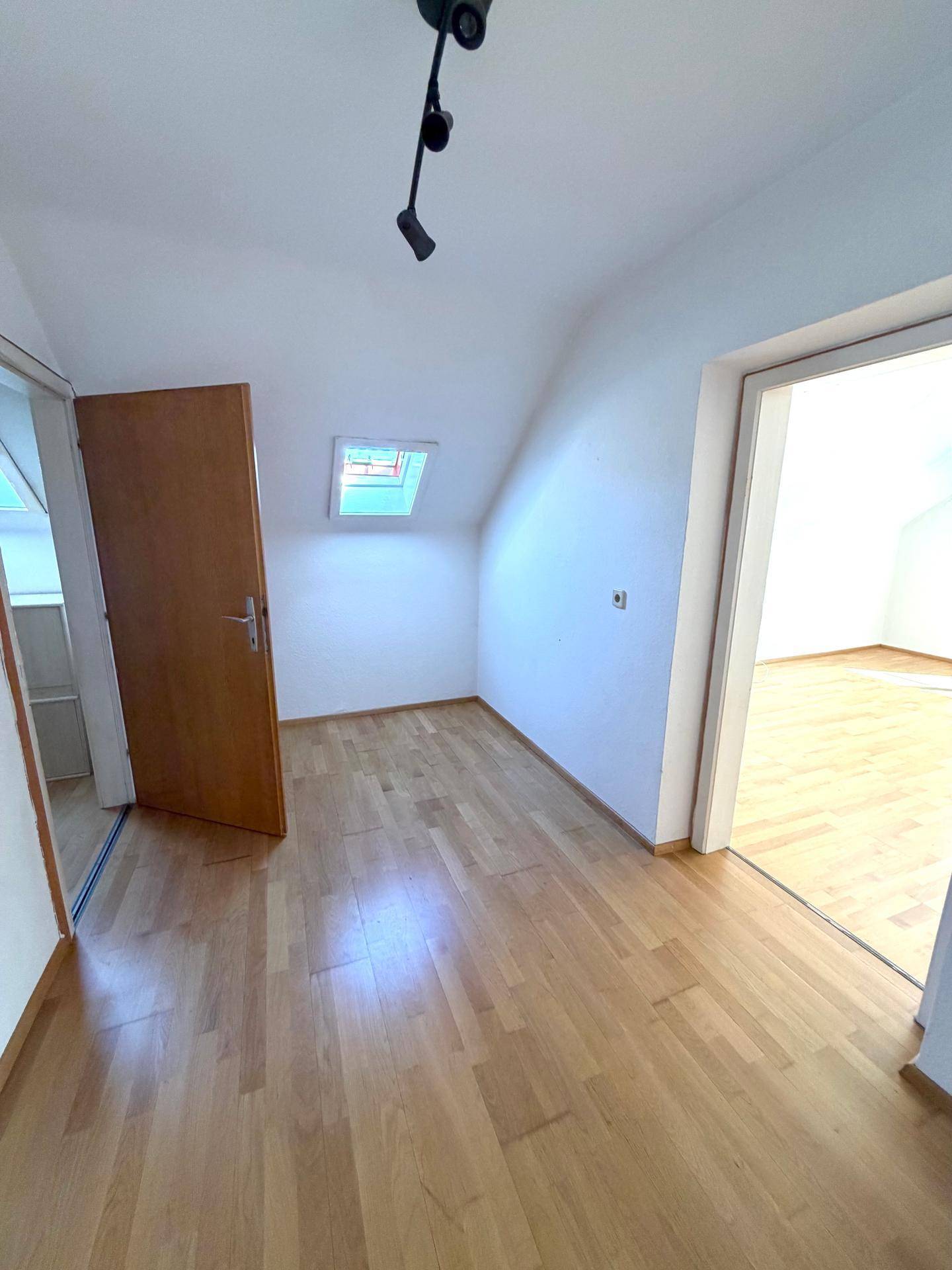 Heller Raum im Dachgeschoss mit Holzboden, Dachfenster und Zugang zu weiteren Zimmern.