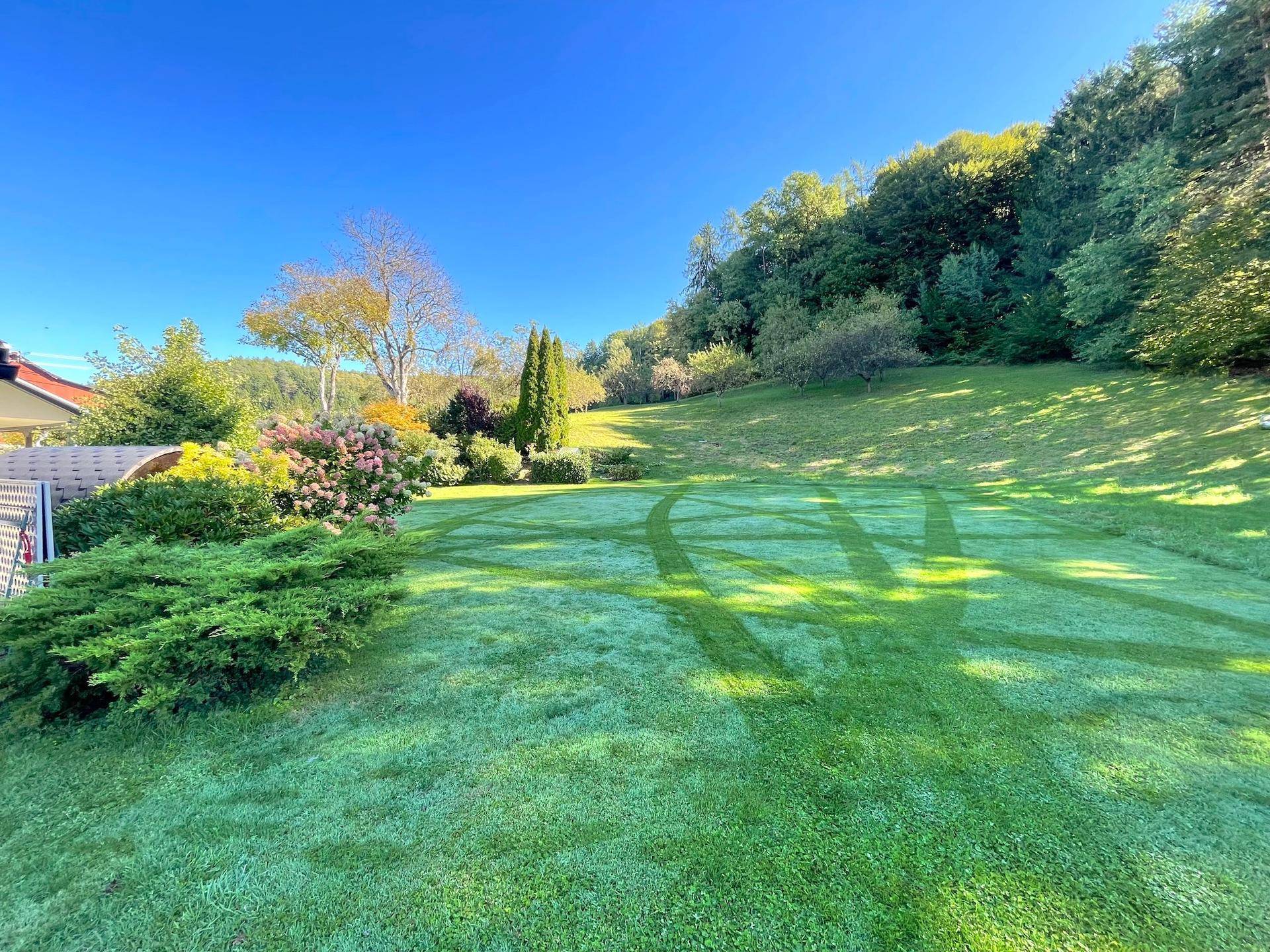 Große, gepflegte Rasenfläche mit Bäumen und Sträuchern, die sich in eine hügelige Landschaft erstreckt.