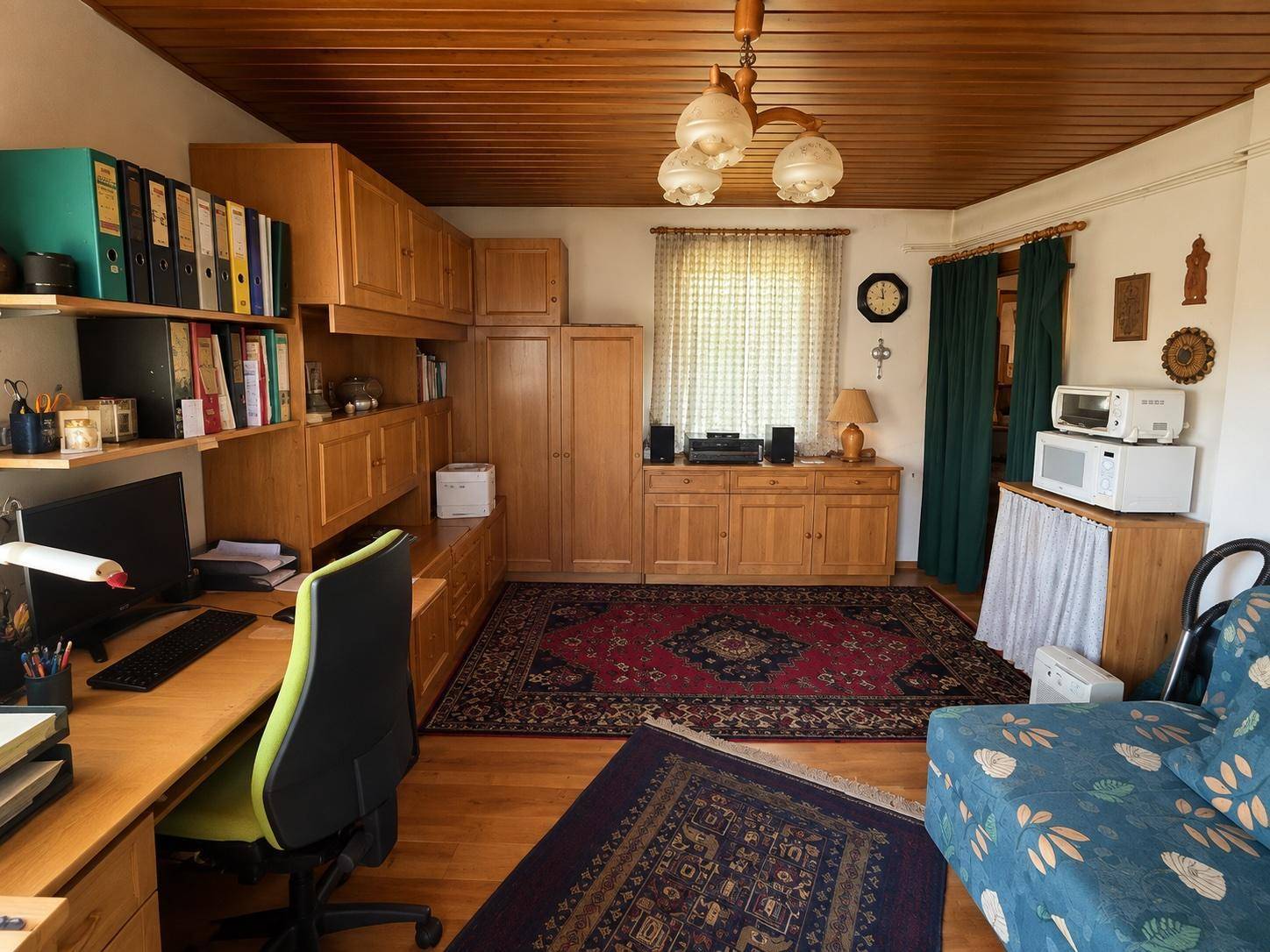 Wohnzimmer mit Holzbalkendecke, Teppichen und einem integrierten Arbeitsbereich mit Schreibtisch.