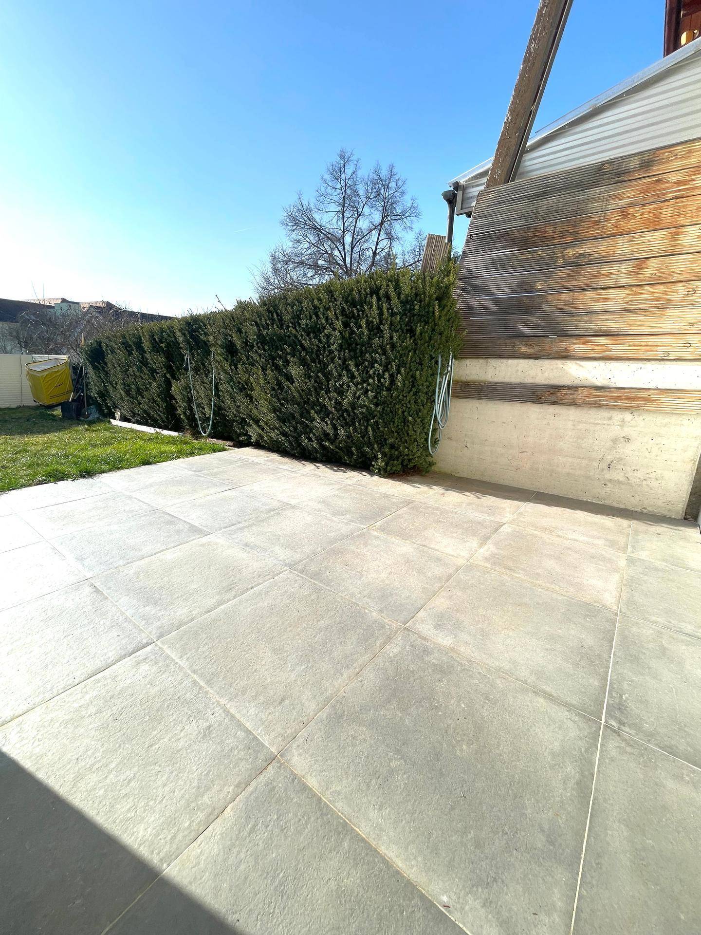 Geräumige geflieste Terrasse mit Hecke, ideal für Entspannung im Freien.