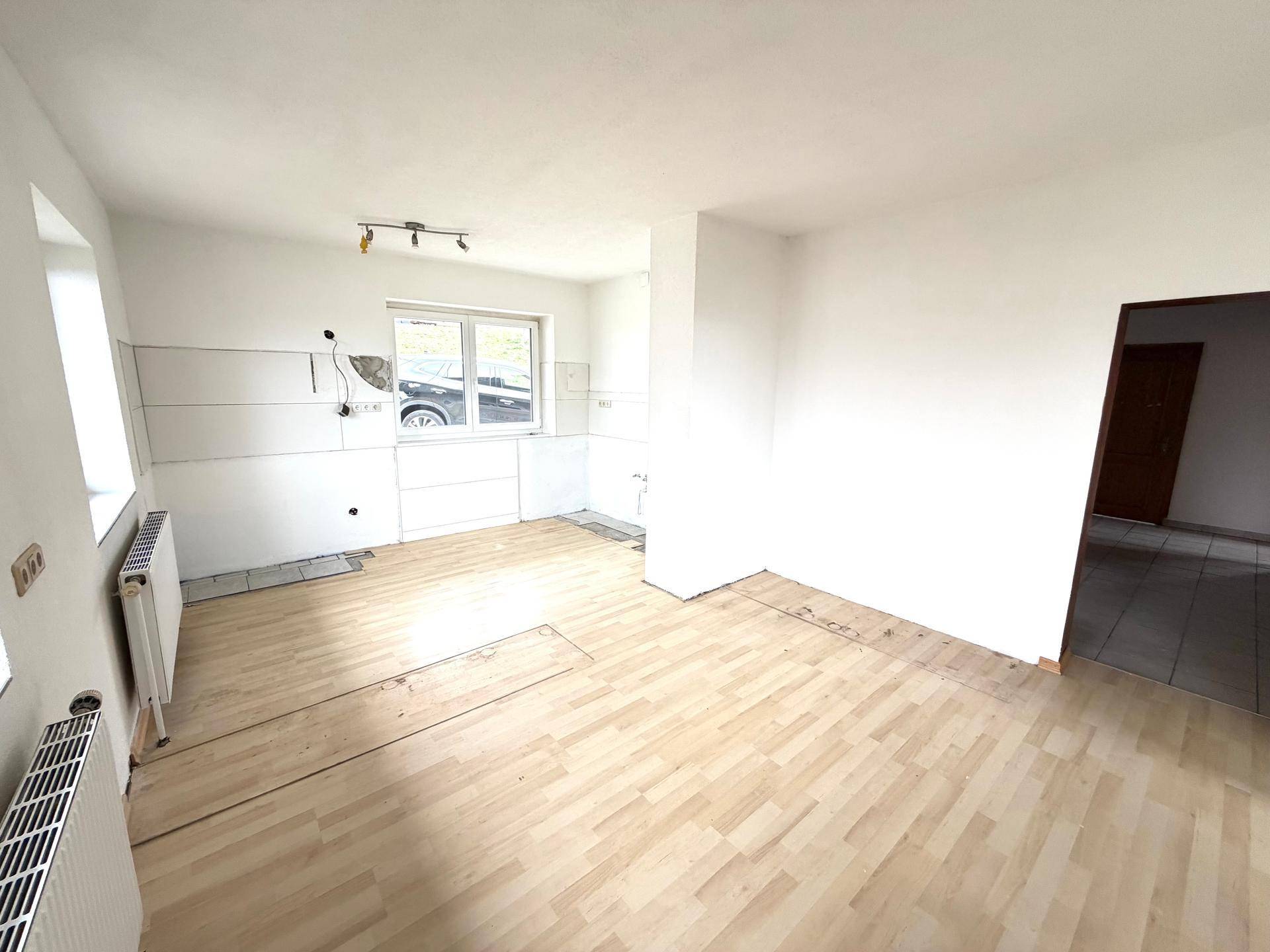 Heller Küchenbereich mit Holzboden und vorbereiteten Anschlüssen für die Küchenzeile, viel Tageslicht.