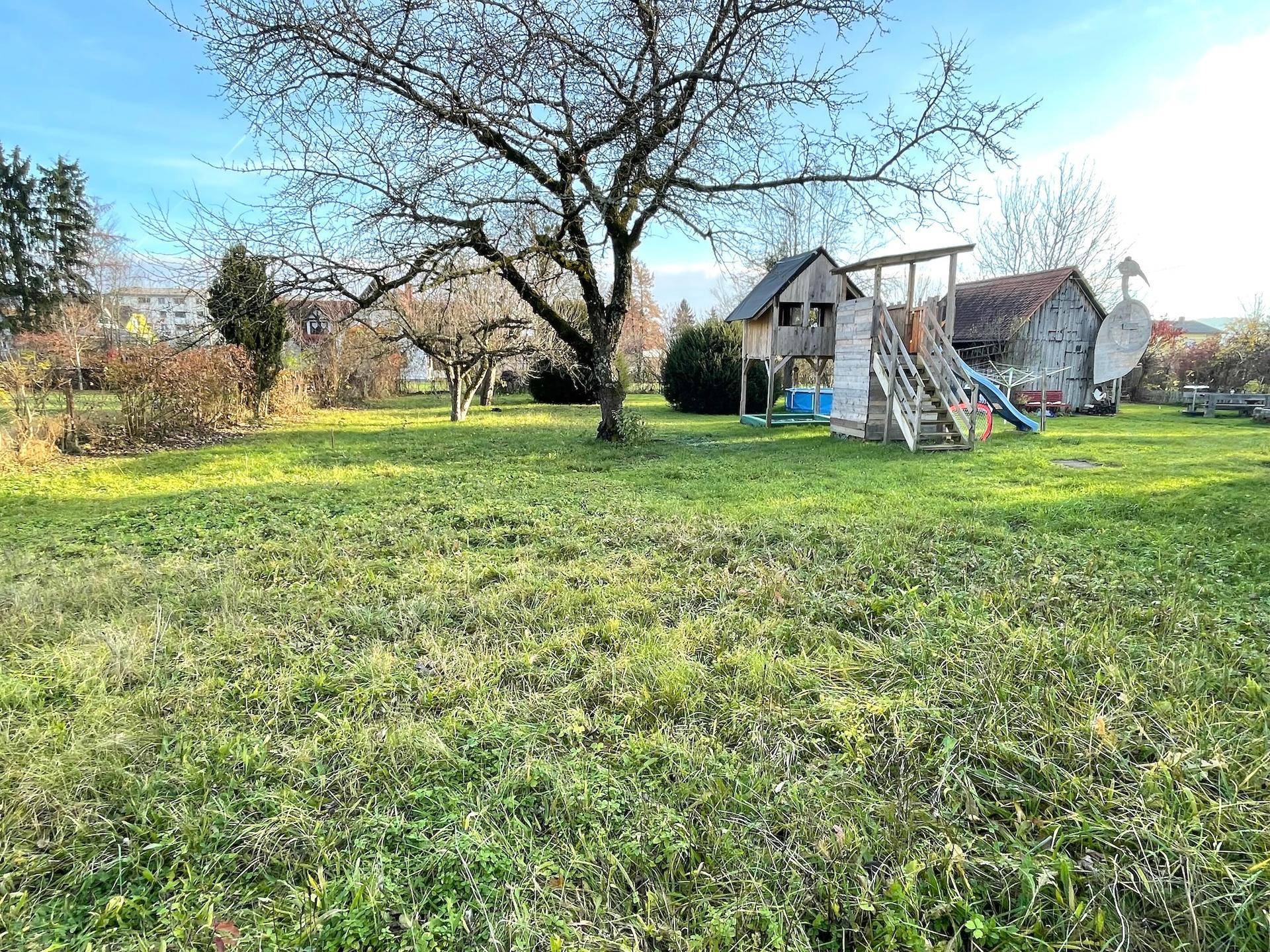 Geräumiger Garten mit einem großen Baum und einem Holzspielplatz für Kinder.
