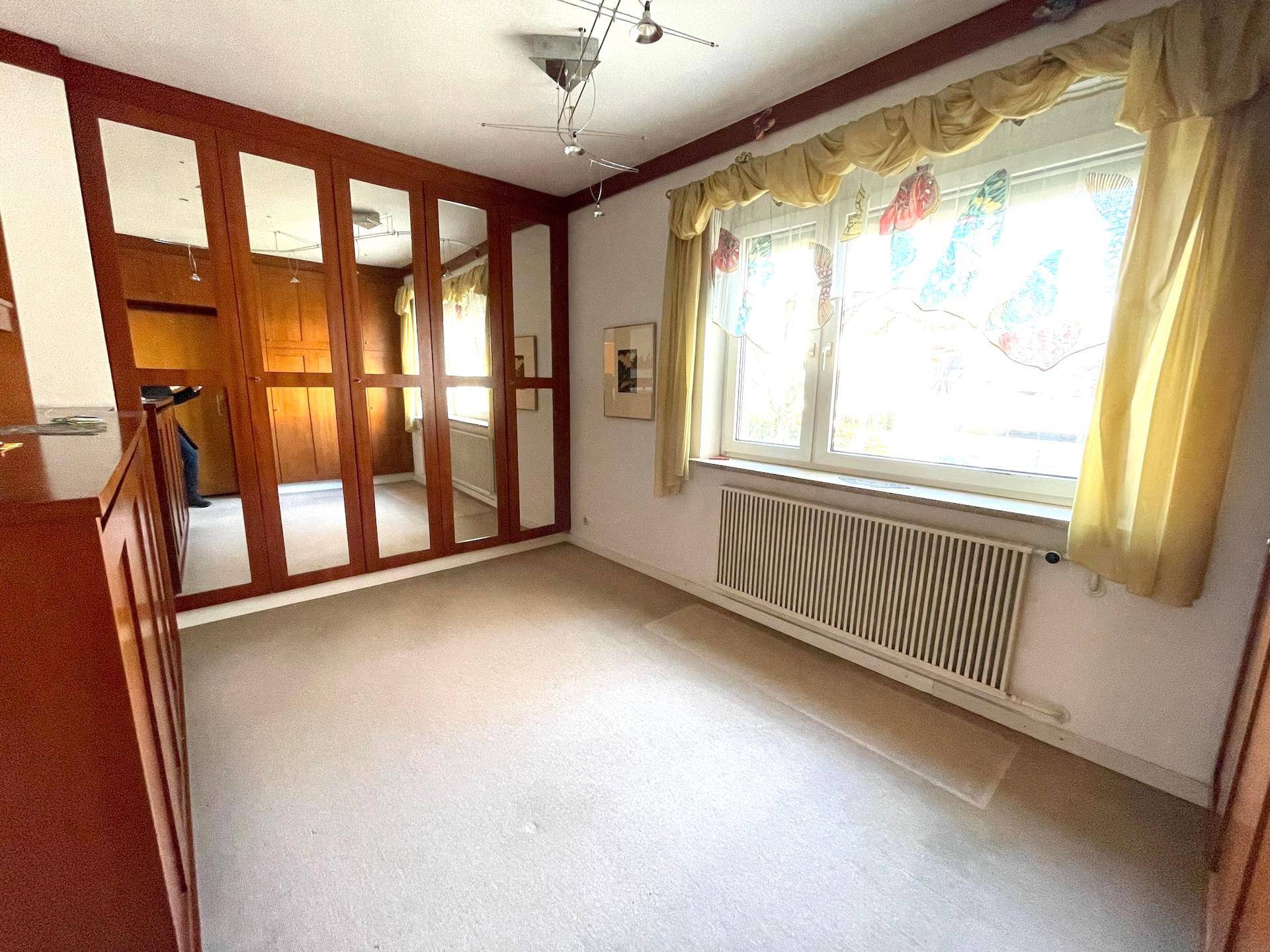 Schlafzimmer mit großem Fenster, Teppichboden und Einbauschränken.
